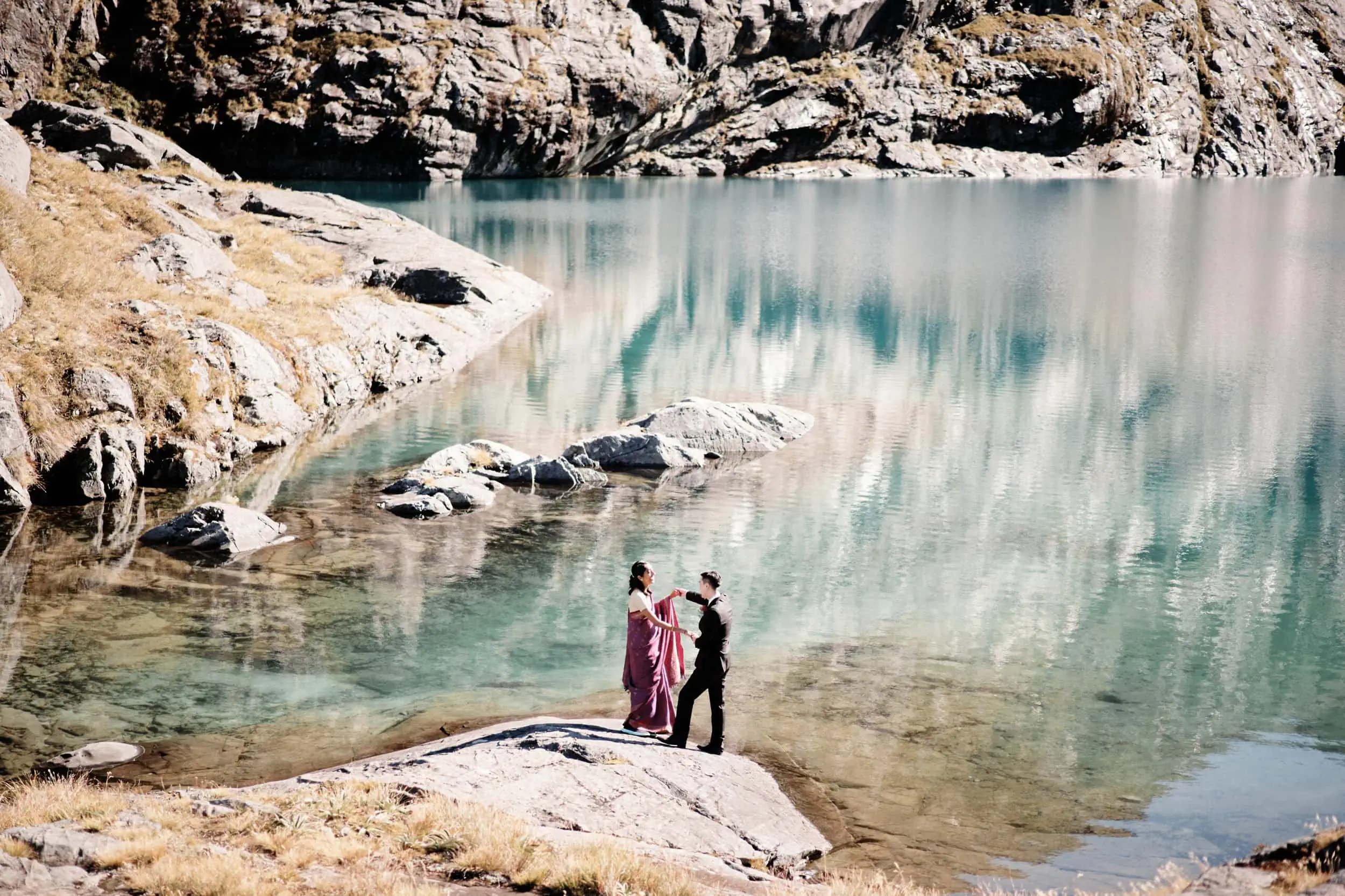 A couple standing on rocks near a lake.