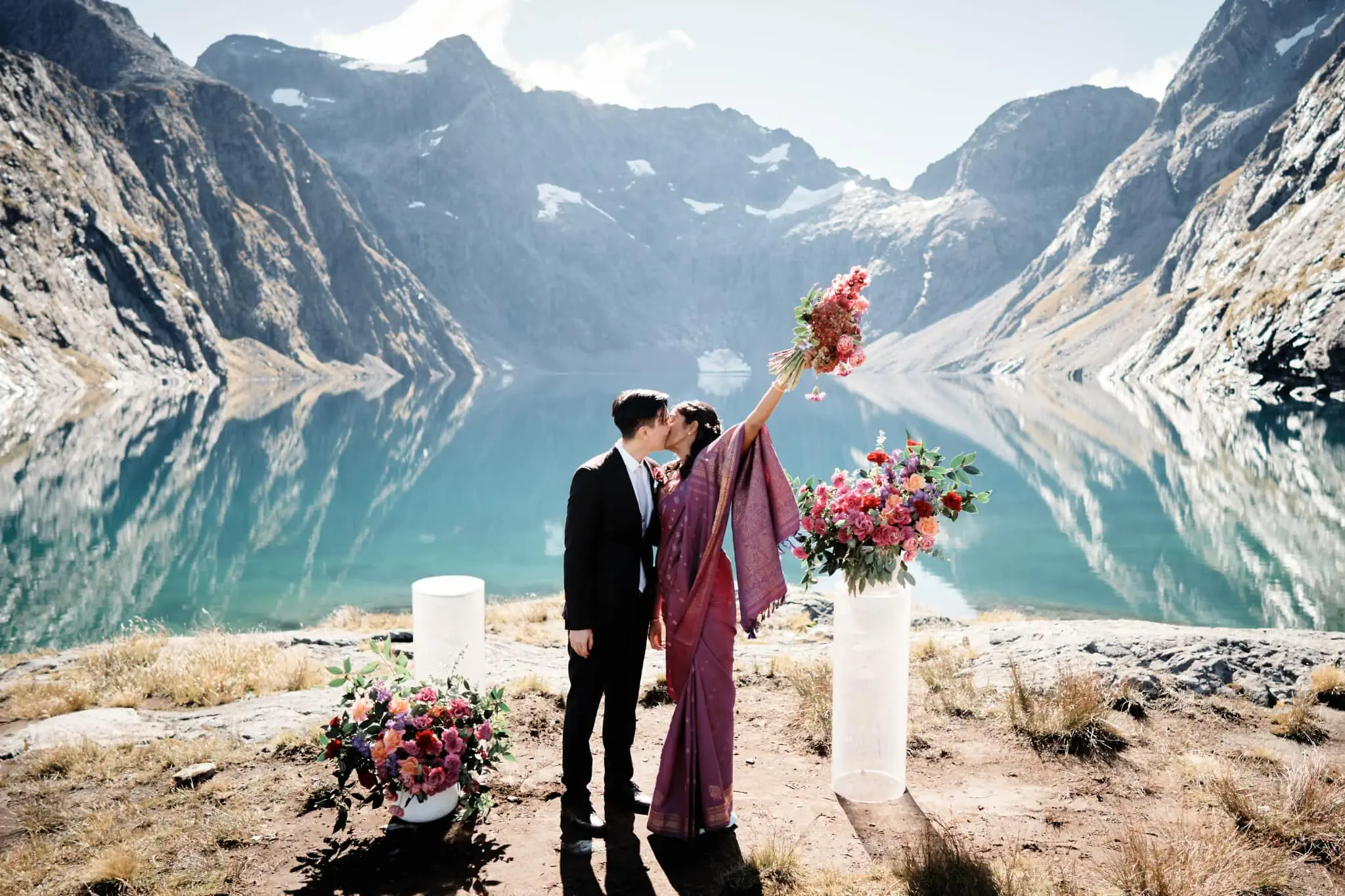 A bride and groom standing in front of a lake.