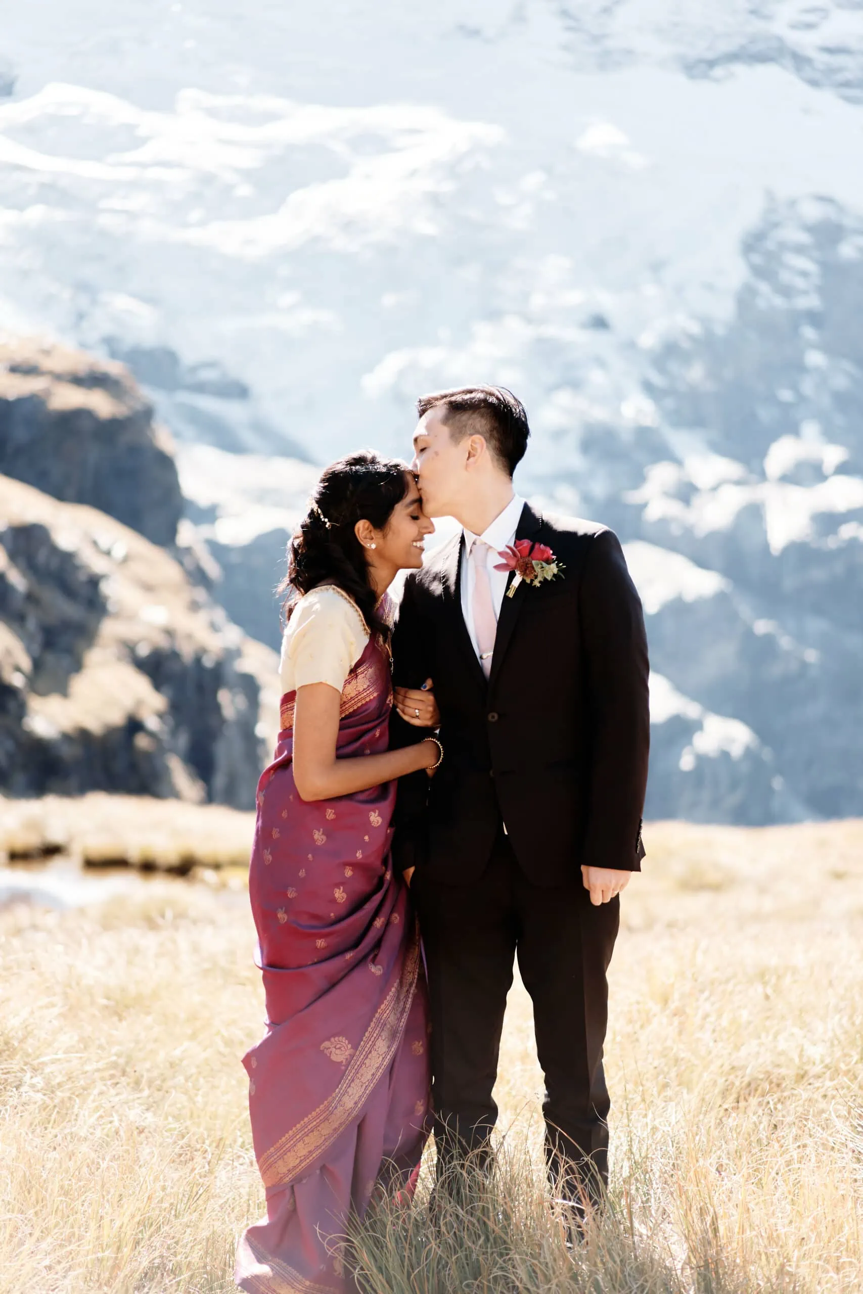 A bride and groom kissing in front of a mountain.