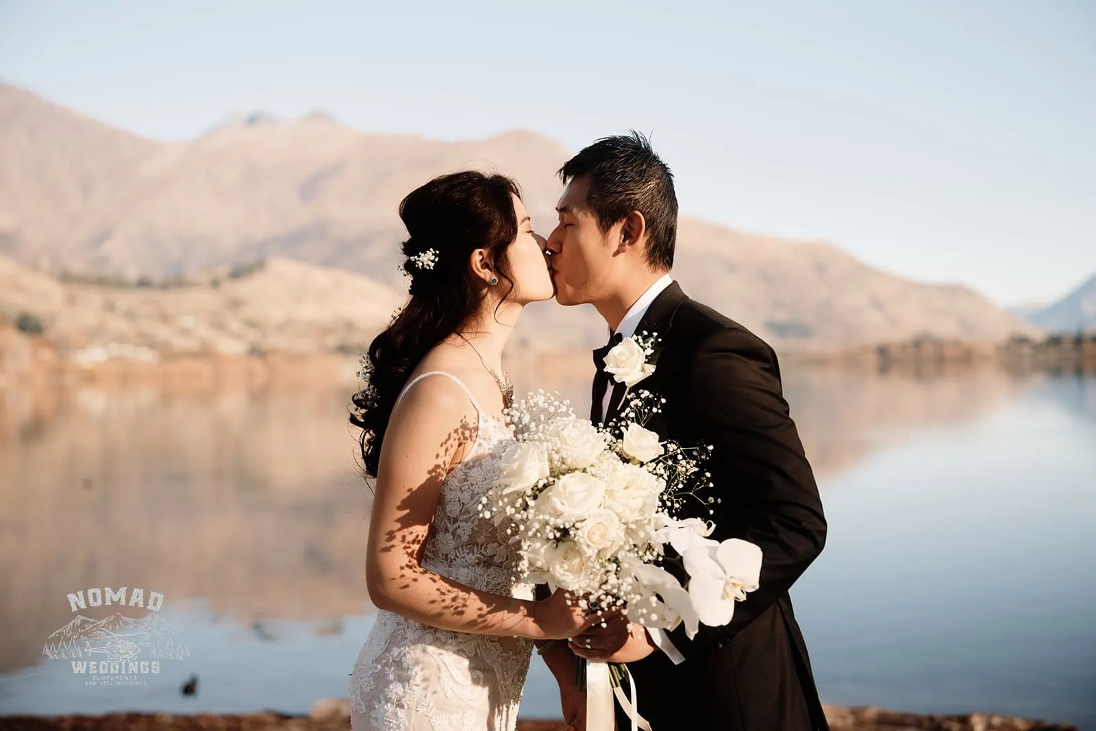 Connie and Andrew share a romantic kiss during their Remarkables Heli pre wedding shoot near a breathtaking lake.