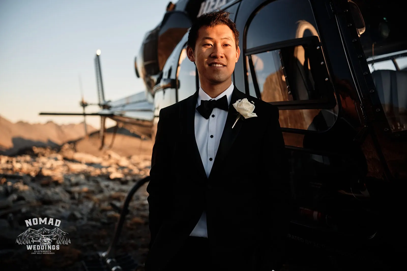 A man in a tuxedo standing next to a helicopter during Connie and Andrew's Remarkables Heli Pre Wedding Shoot.