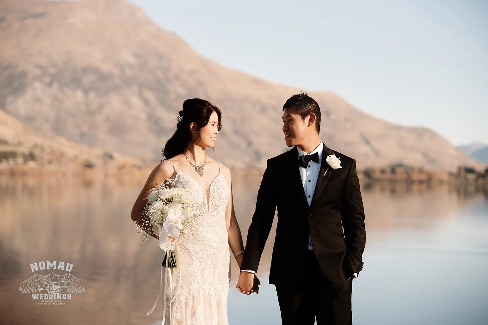 Connie and Andrew celebrating their love with a captivating Pre Wedding Shoot by The Remarkables Heli, near a serene lake, while holding hands.