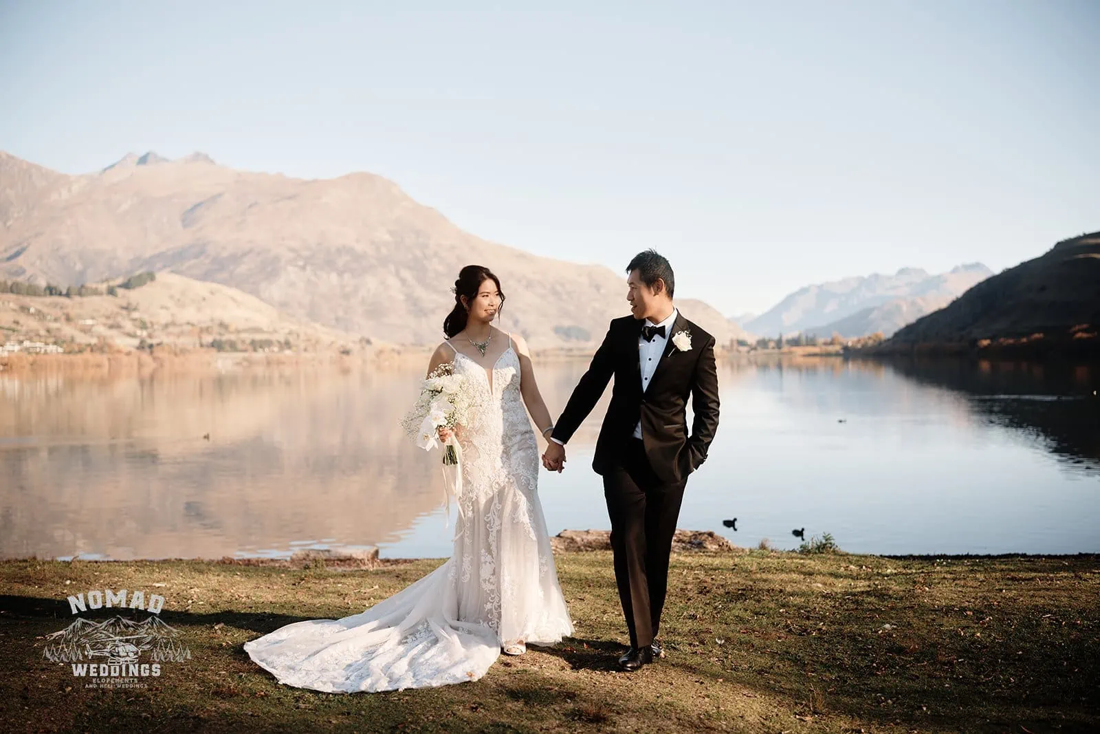 Connie and Andrew's Remarkables Heli Pre Wedding Shoot captures them standing in front of a lake with mountains in the background.