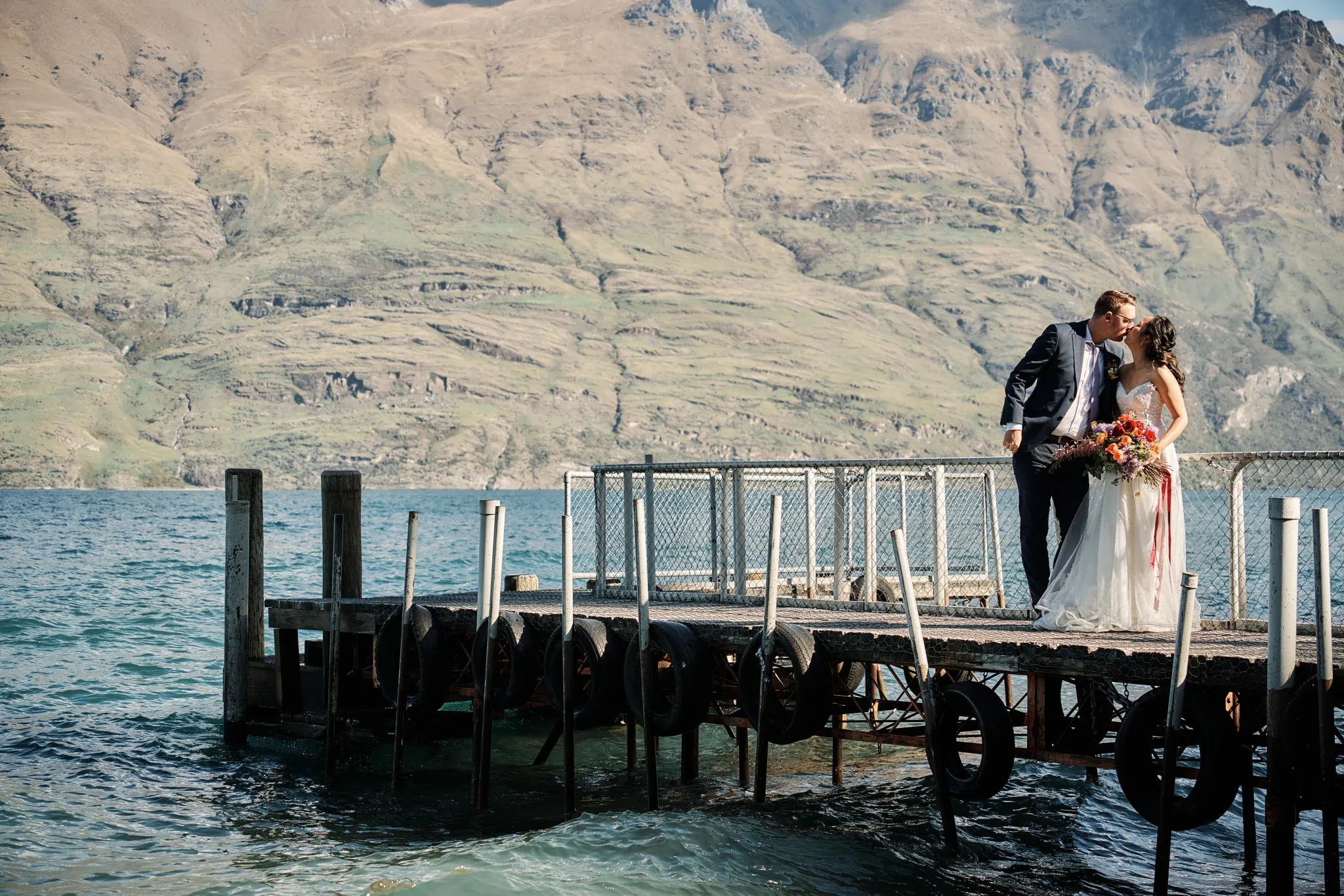Ace and Alex's pre wedding shoot at Moke Lake, with a bride and groom standing on a dock in front of mountains.
