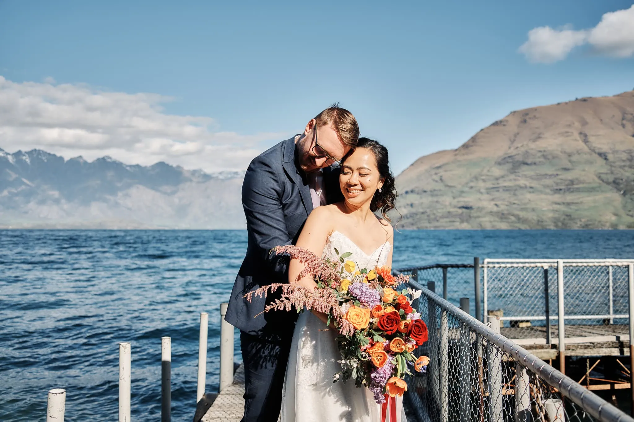 Ace and Alex's pre wedding shoot at Moke Lake, with a bride and groom standing on a dock and mountains in the background.