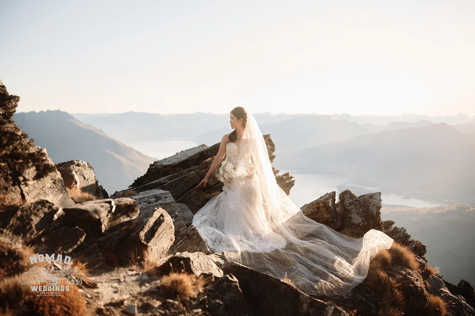 Connie and Andrew capture picturesque moments during their Remarkables Heli pre-wedding shoot, with the bride sitting atop a mountain admiring Lake Wanaka.