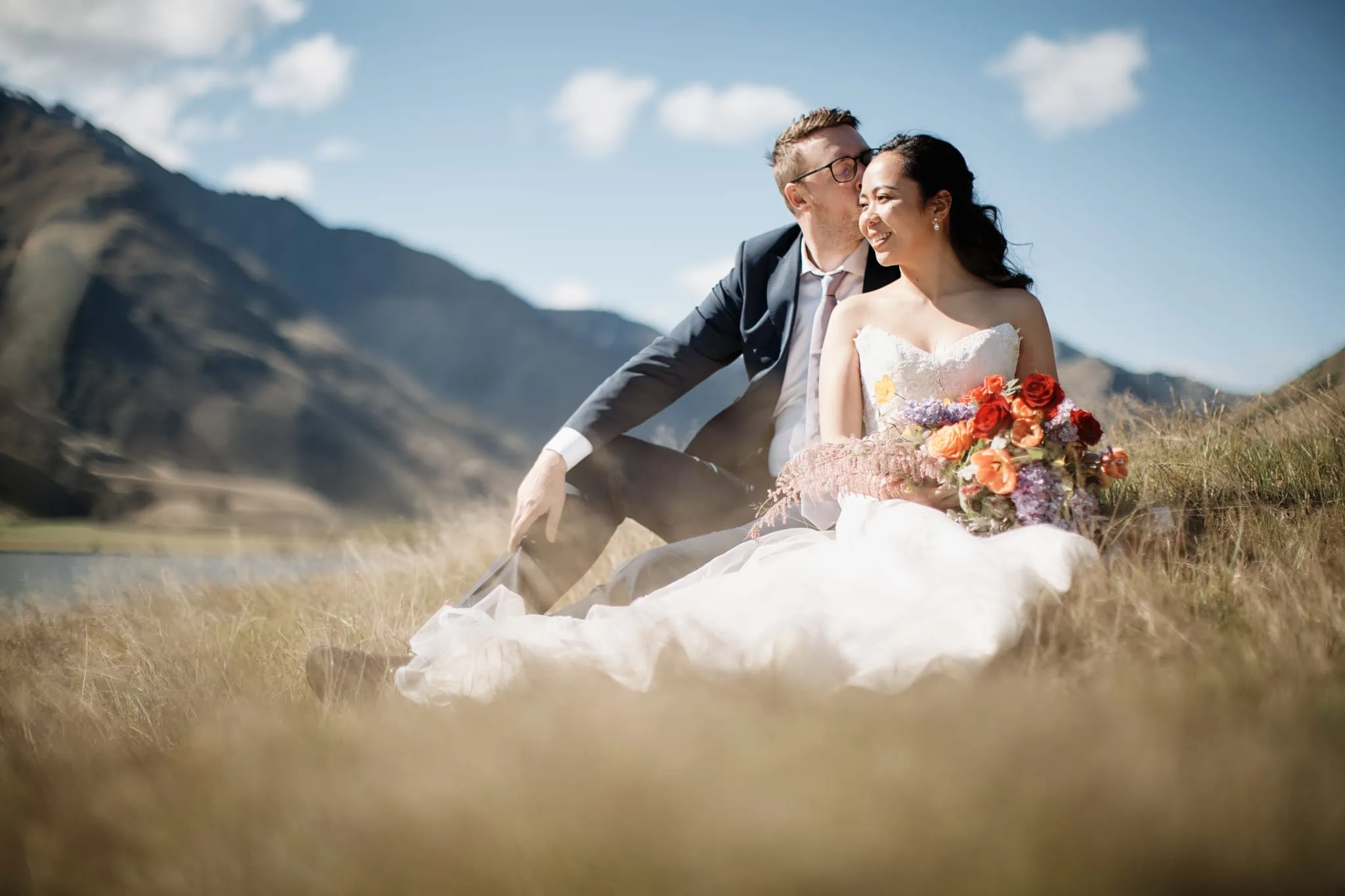 Ace and Alex's pre wedding shoot at Moke Lake, as they sit in a grassy field against the stunning backdrop of mountains.