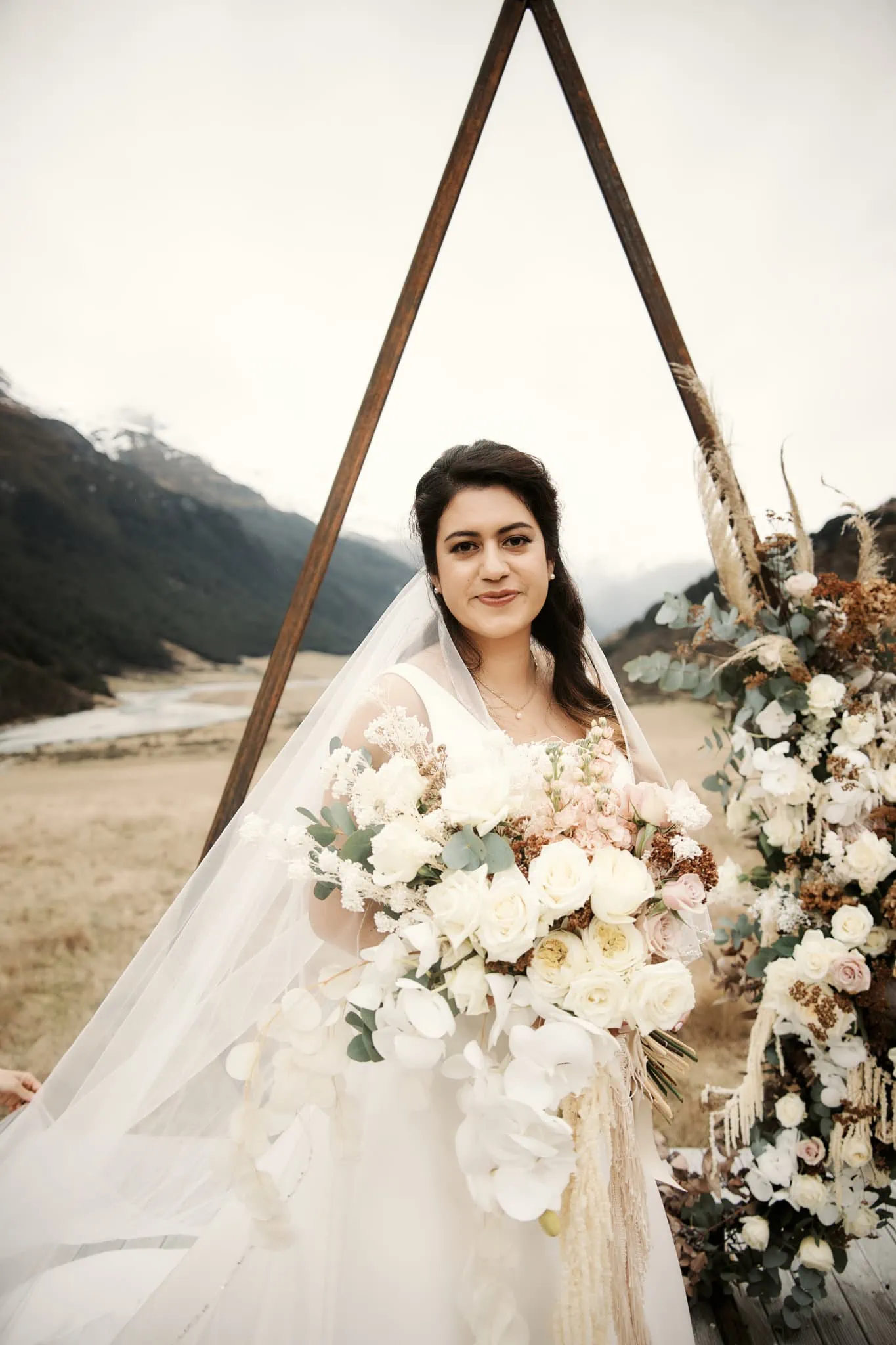 Michelle, wearing a white wedding dress, stands in front of a mountain during her Rees Valley Station elopement wedding with Vedran.