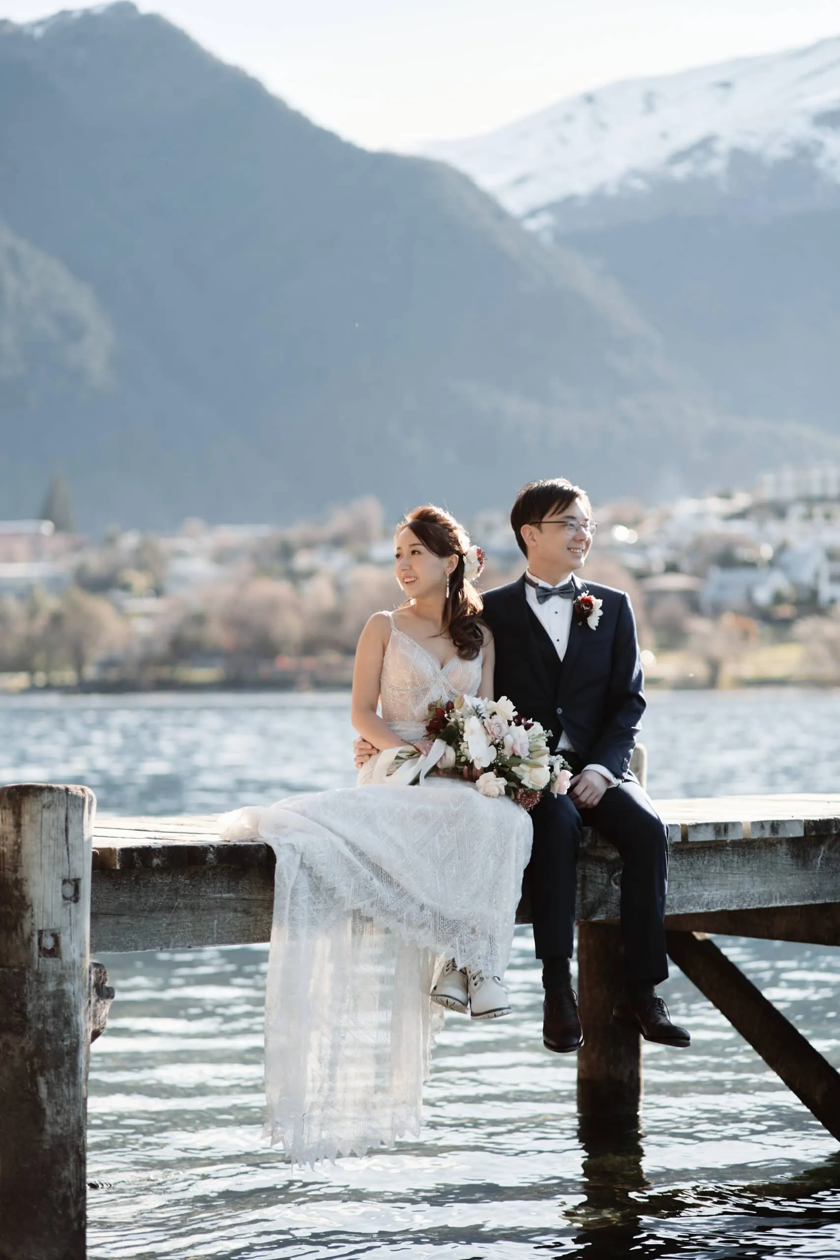 A couple sitting on a dock with mountains in the background for Stephanie & Carven's Heli Pre Wedding Elopement at The Remarkables.