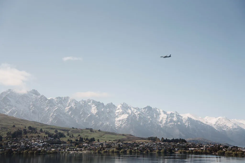 Felicia & Kent's pre-wedding shoot captures a plane flying over a lake with mountains in the background in Queenstown, NZ.