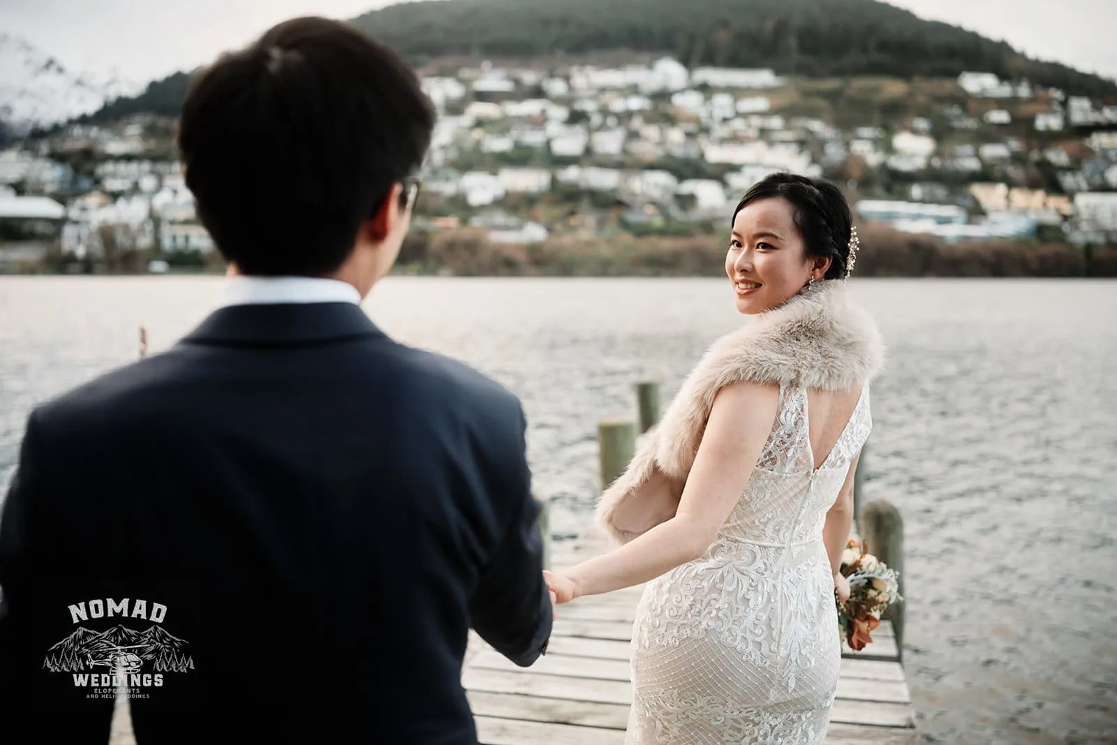 Joanna and Tony, a bride and groom, have their pre-wedding shoot on a dock with mountains in the background in Queenstown, New Zealand.