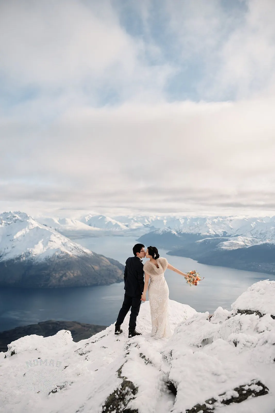 Joanna and Tony, a bride and groom, standing on top of a snow covered mountain in Queenstown, New Zealand during their pre-wedding shoot.