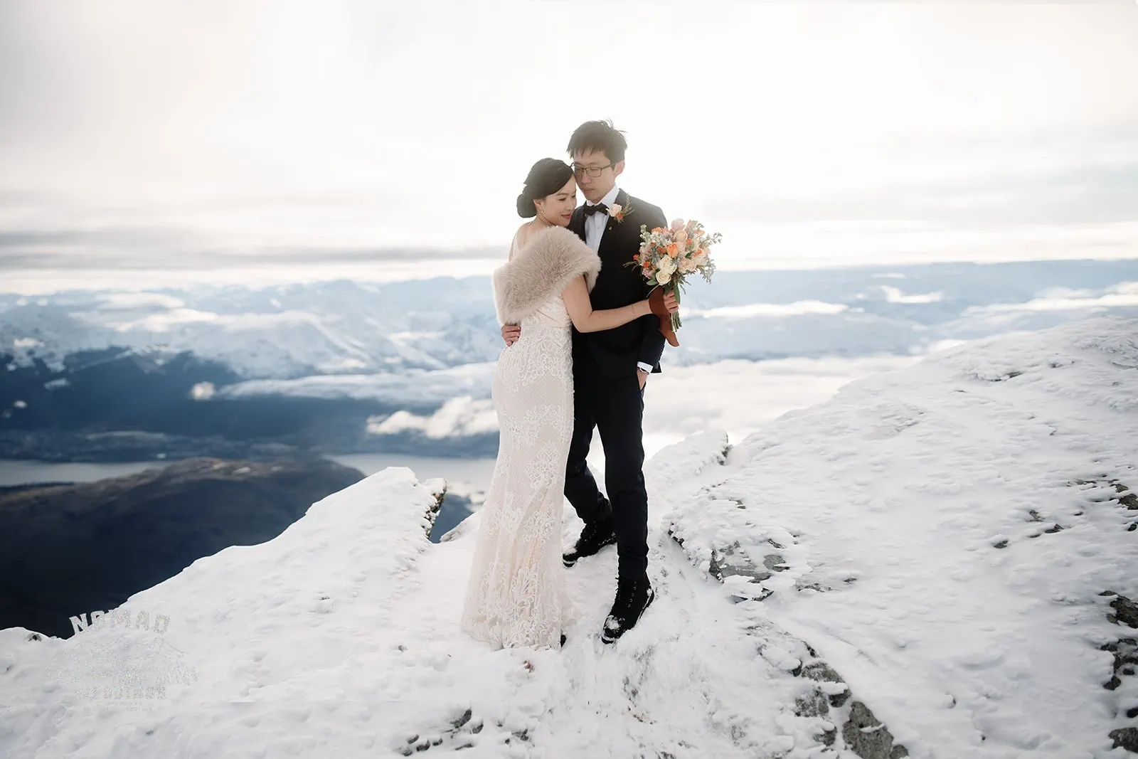 Joanna and Tony, a bride and groom, posing for their pre-wedding shoot on top of a snow-covered mountain in Queenstown, New Zealand.