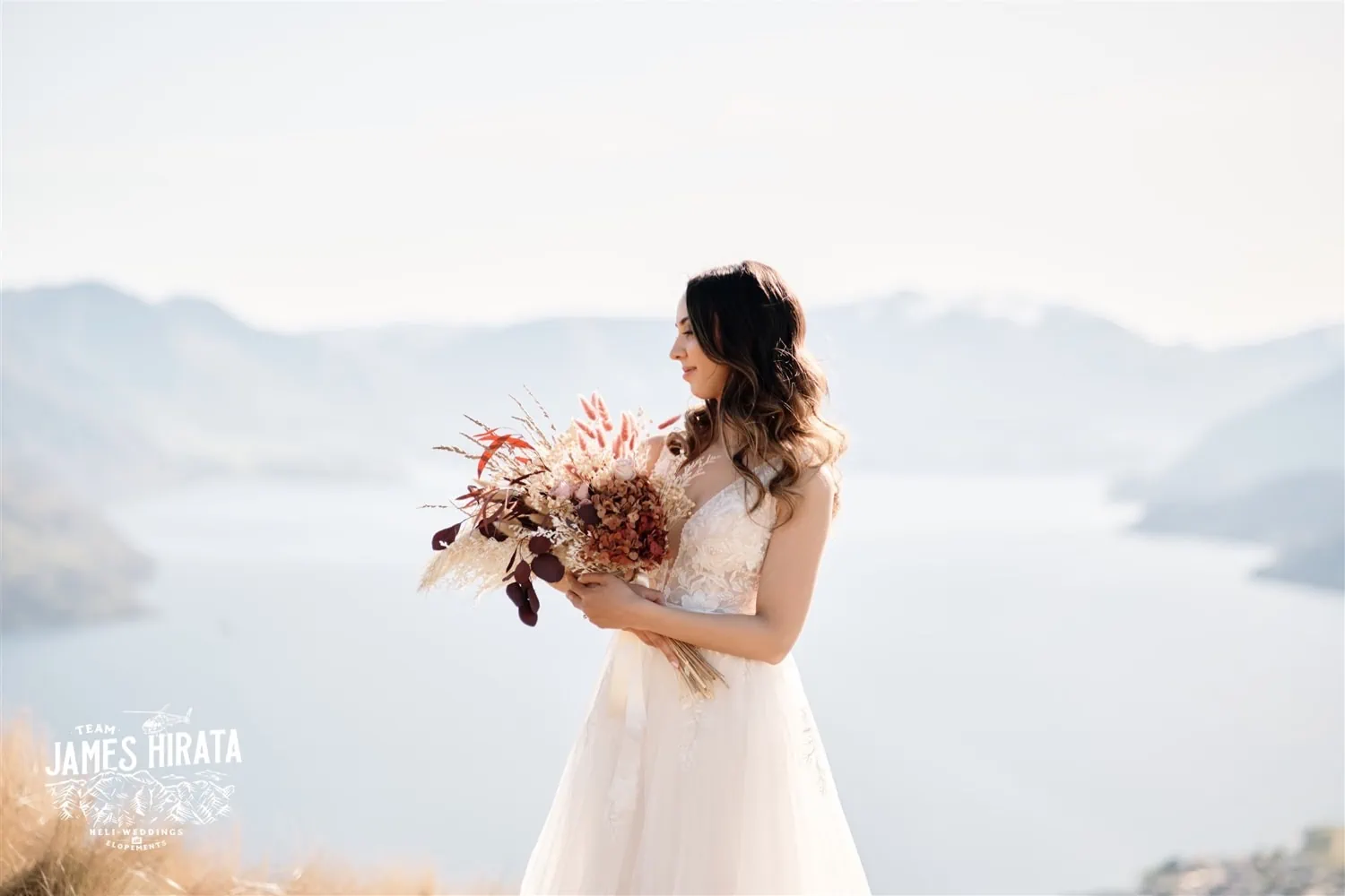 A New Zealand bride standing atop a mountain at Lake Wakatipu during Isabelle and Vilay's elopement wedding in Queenstown.