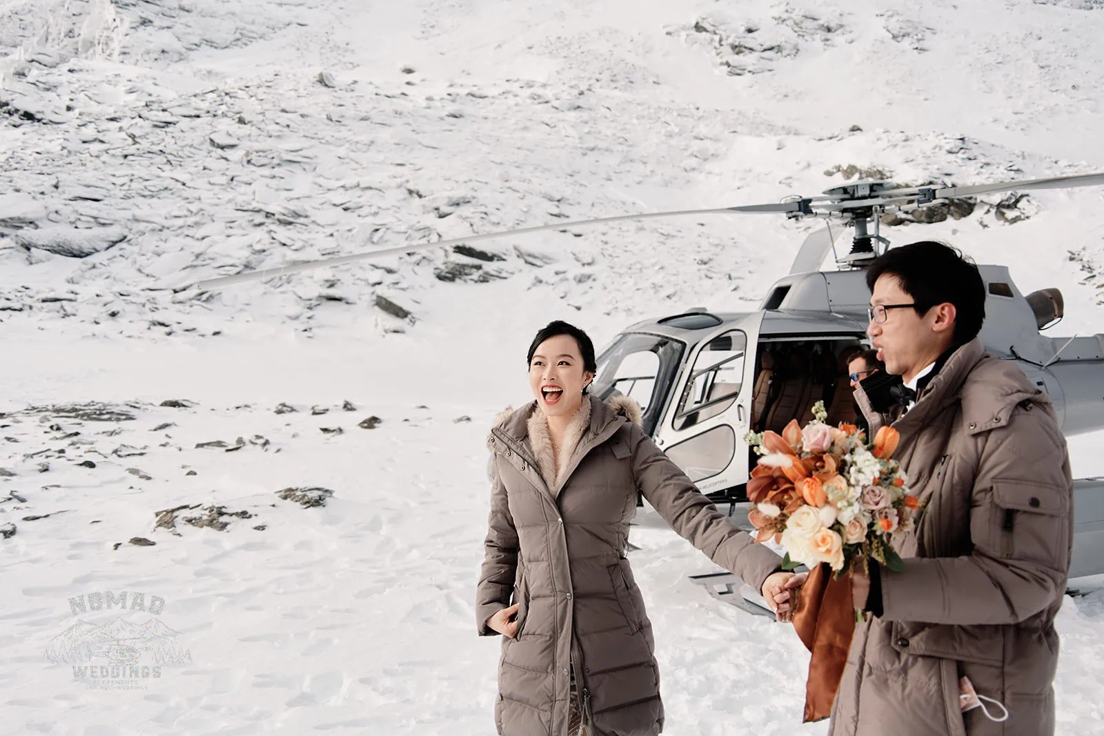 A pre-wedding shoot in Queenstown, New Zealand, featuring Joanna and Tony standing next to a helicopter in the snowy landscape.