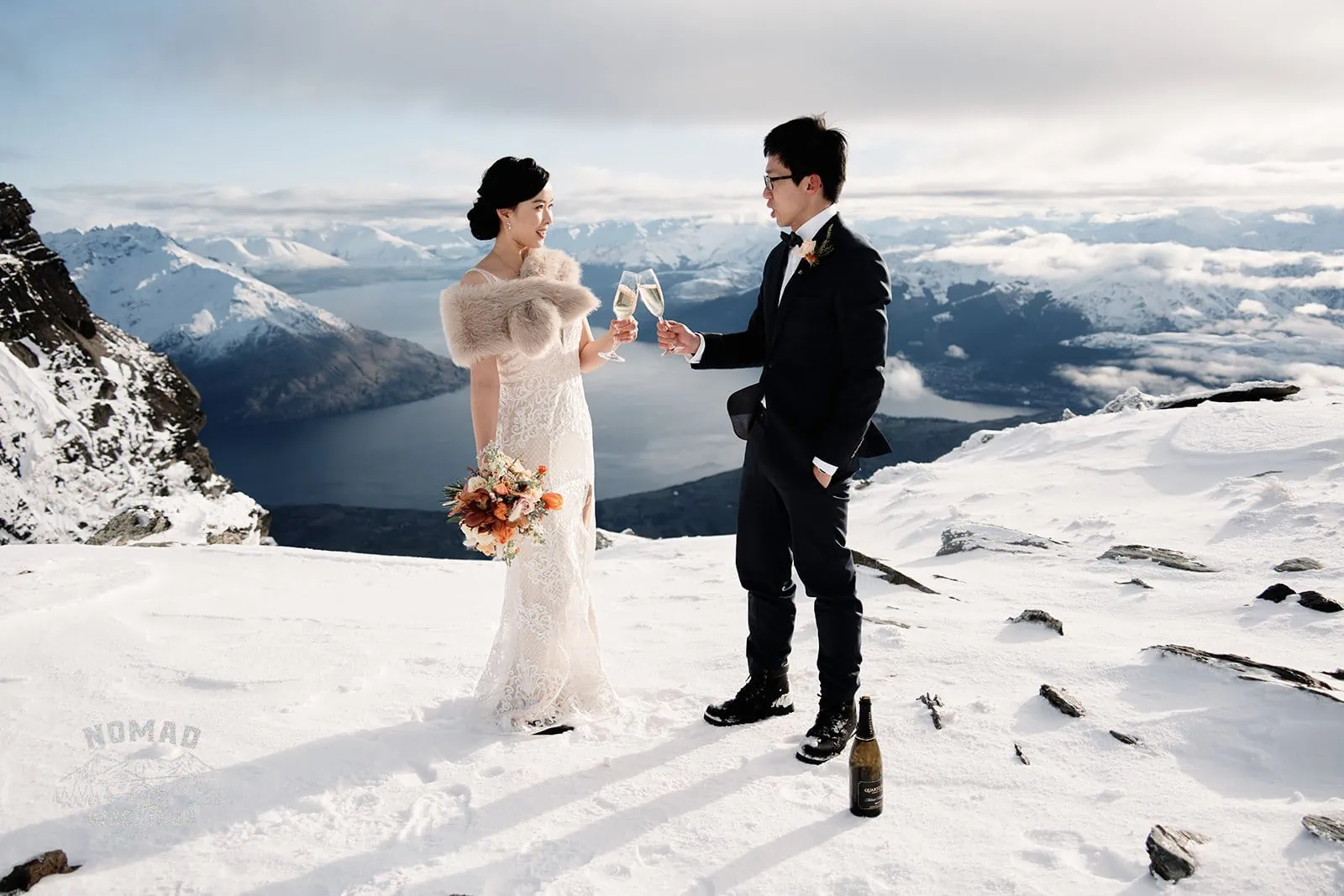 Joanna and Tony having a pre-wedding shoot, toasting champagne on top of a snowy mountain in Queenstown, New Zealand.