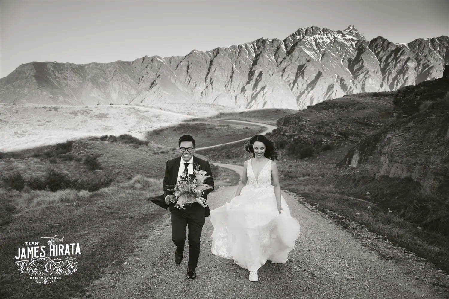 A couple's elopement wedding in Queenstown, New Zealand, featuring a bride and groom walking down a dirt road with mountains in the background.