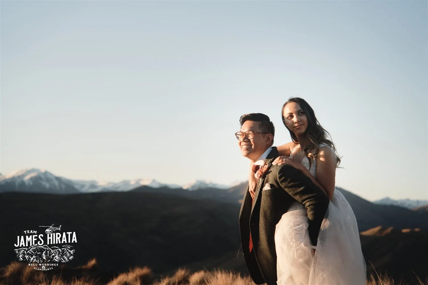 Bride and groom atop hill with mountains in Queenstown, New Zealand.