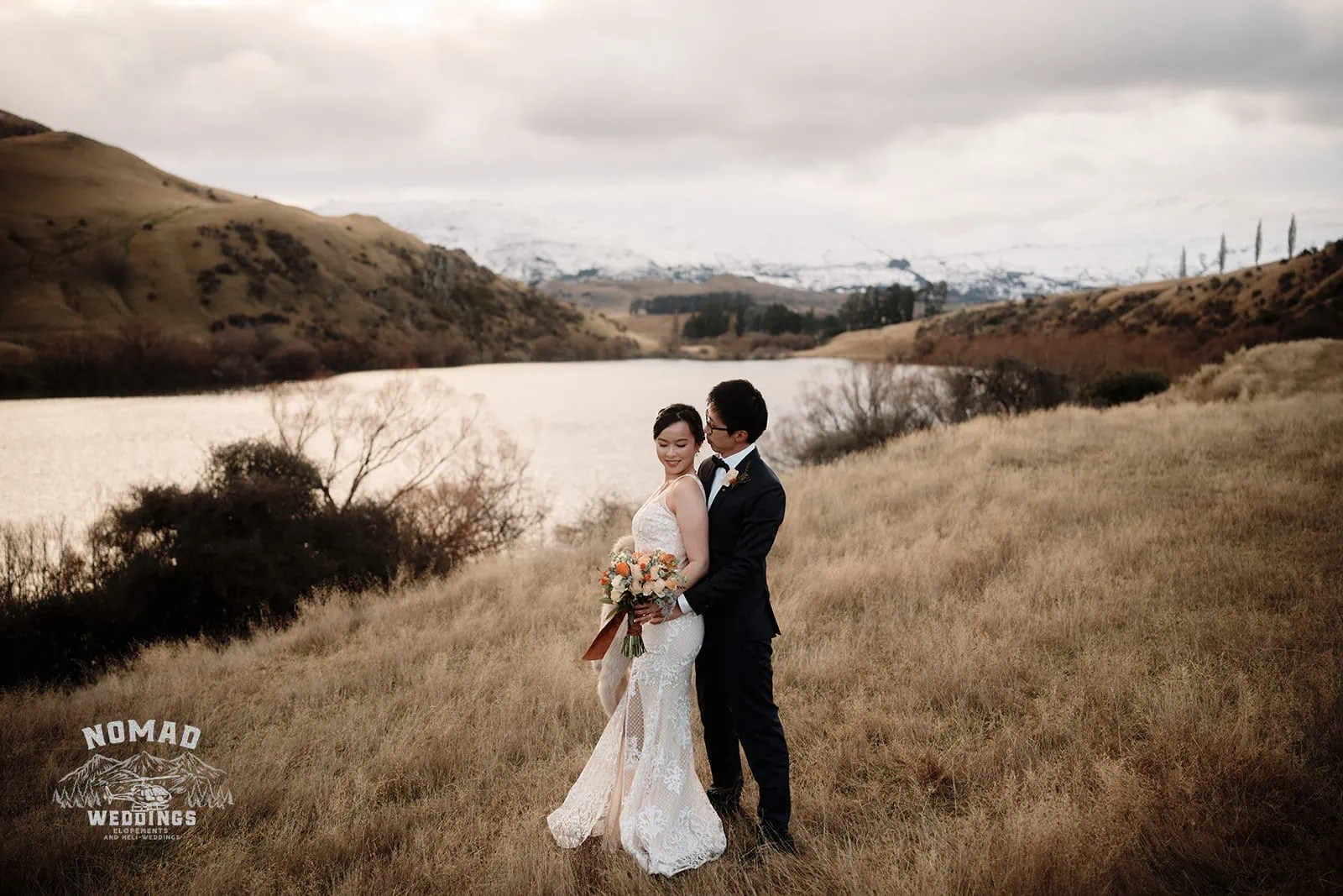 Joanna and Tony posing for their pre-wedding shoot in the scenic fields near a lake in Queenstown, New Zealand.