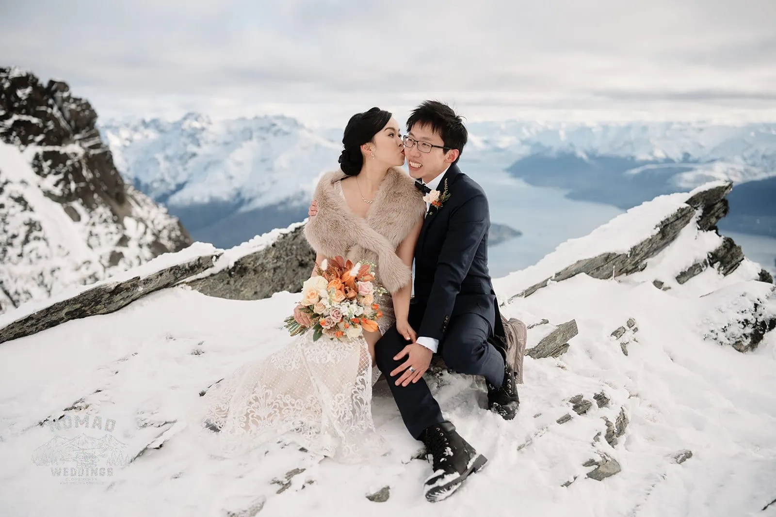 Joanna and Tony, a bride and groom, pose on top of a snow-covered mountain during their pre-wedding shoot in Queenstown, New Zealand.