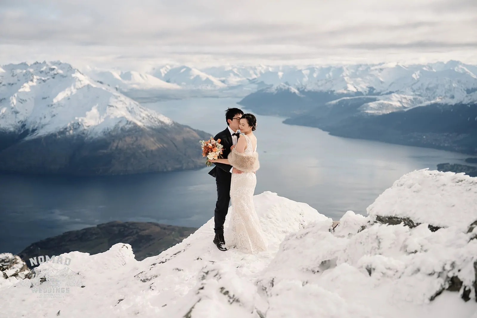 Joanna and Tony, a bride and groom, posing during their pre-wedding shoot on a mountain overlooking Lake Wanaka in Queenstown, New Zealand.