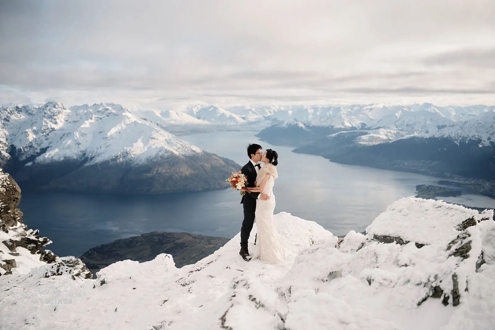 A bride and groom, Joanna and Tony, posing on a mountain in Queenstown overlooking Lake Wanaka during their pre-wedding shoot in New Zealand.