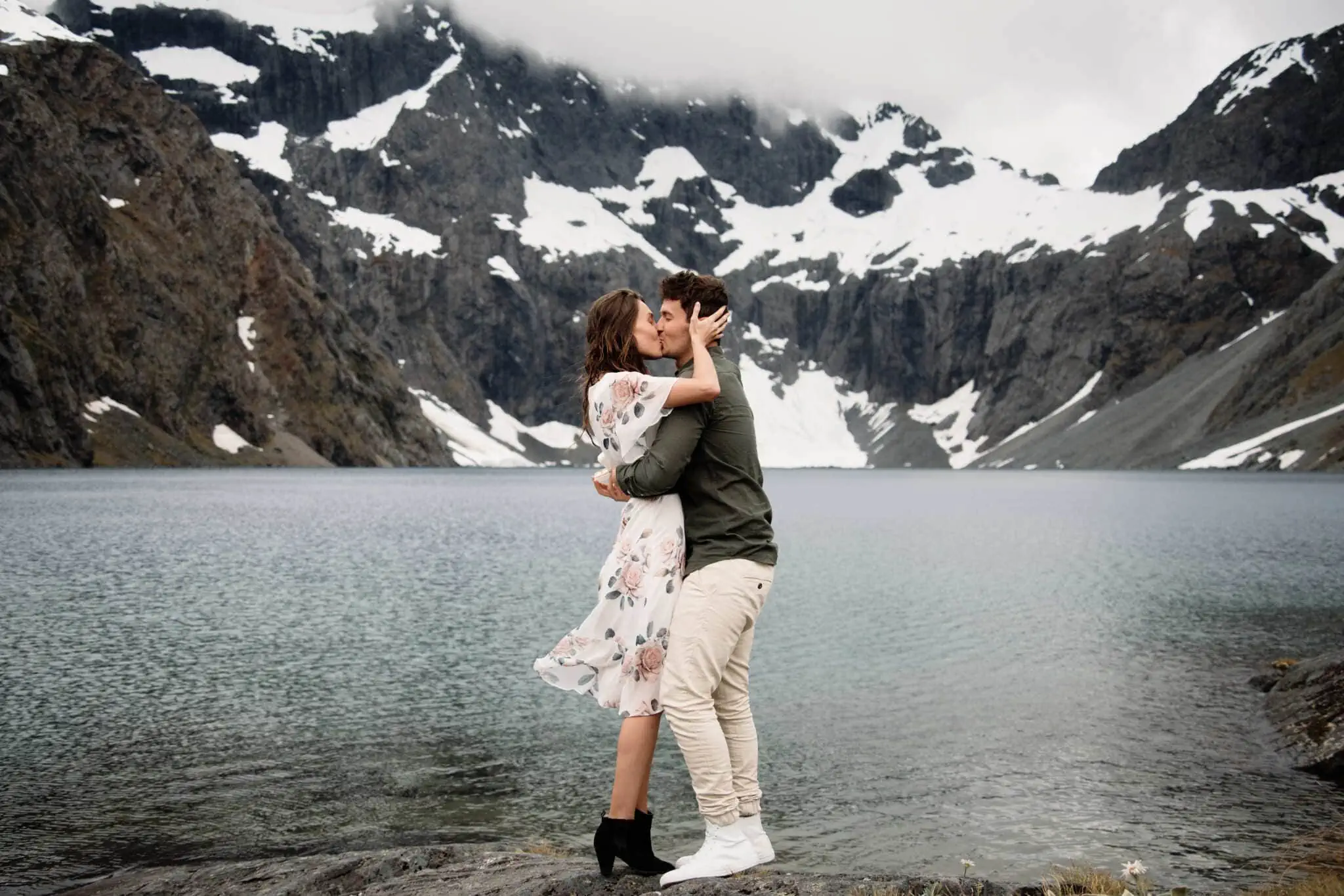 Scott and Hayley embracing in front of a mountain lake.