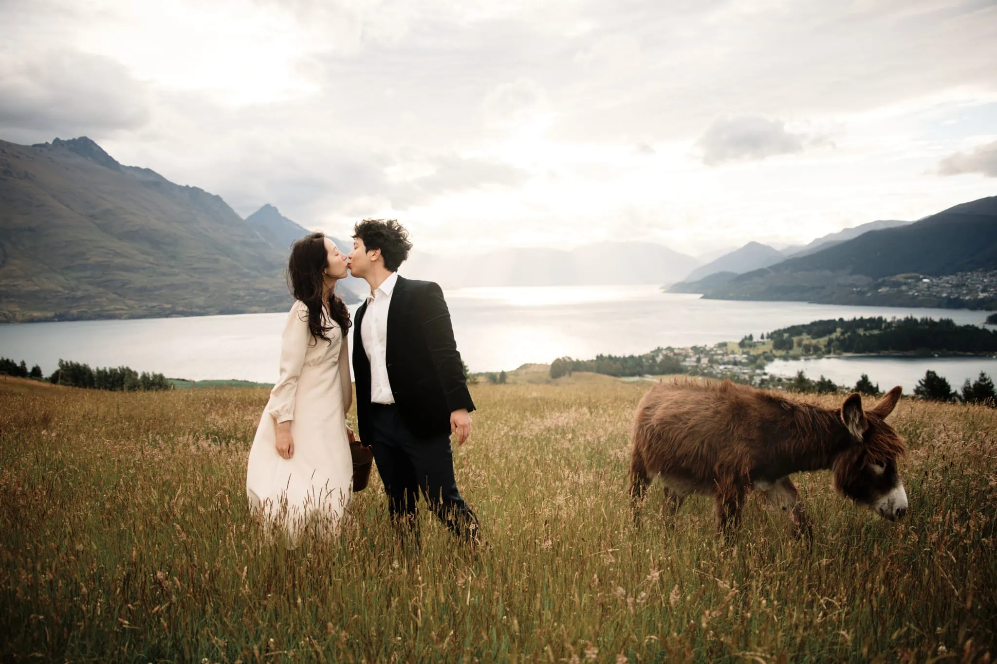 James and Lucy kissing in a field with a donkey.
