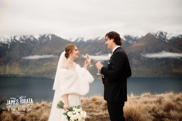 Hannah and Ross, toasting at their elopement wedding in Queenstown, New Zealand with a breathtaking mountain backdrop.