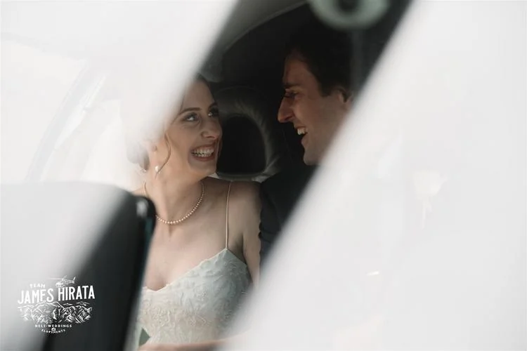 Newlywed couple, Hannah and Ross, beaming with joy in the back seat of a car during their elopement wedding in Queenstown, New Zealand.
