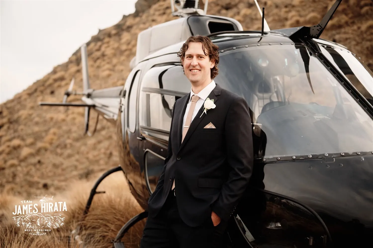A man in a suit standing next to a helicopter during his Queenstown New Zealand elopement wedding.
