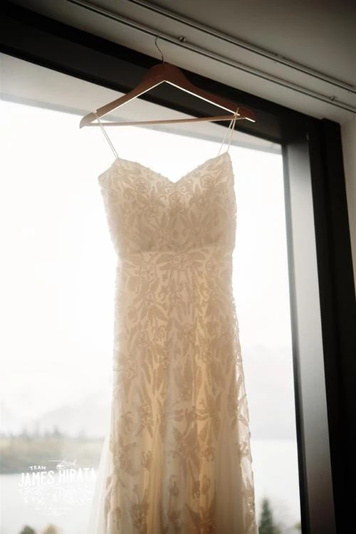 A Queenstown New Zealand elopement wedding dress hanging on a hanger in front of a window.