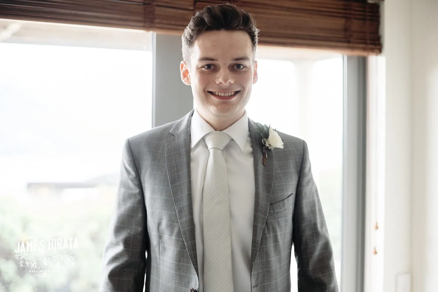 Regan, Jake, Queenstown Elopement Wedding: A man in a suit is smiling in front of a window.