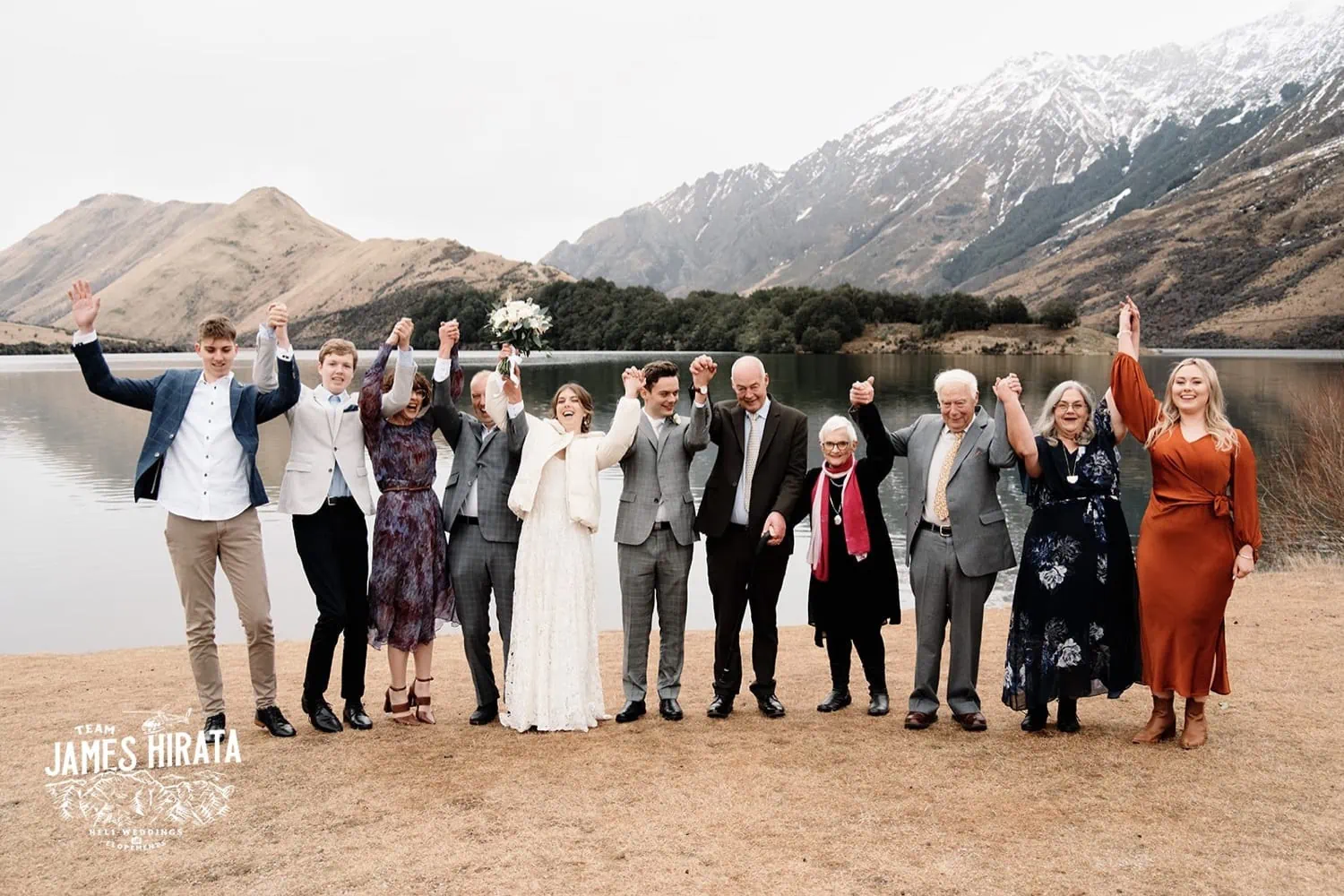 Regan & Jake's Queenstown elopement wedding featuring a group standing in front of a lake with mountains as the backdrop.