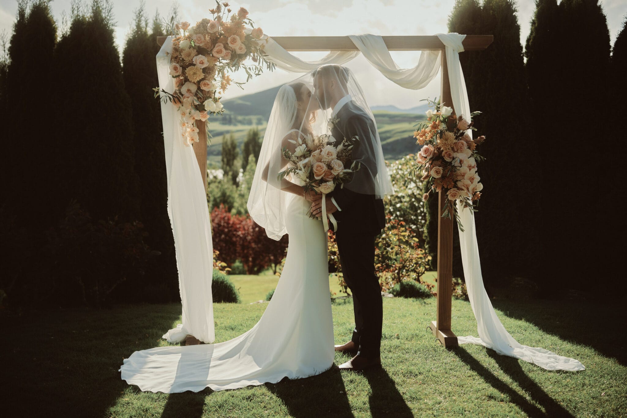 Queenstown New Zealand Elopement Wedding Photographer - A bride and groom kissing under a wedding arch at Stoneridge Estate.