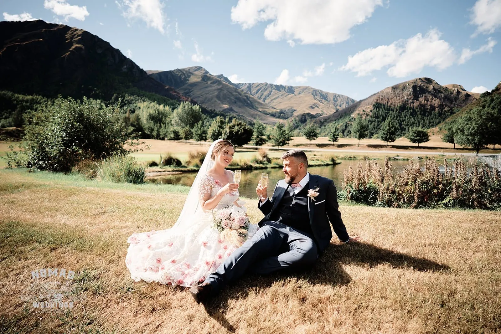 Queenstown New Zealand Elopement Wedding Photographer - A bride and groom sitting on the grass in front of mountains in Queenstown's summer.