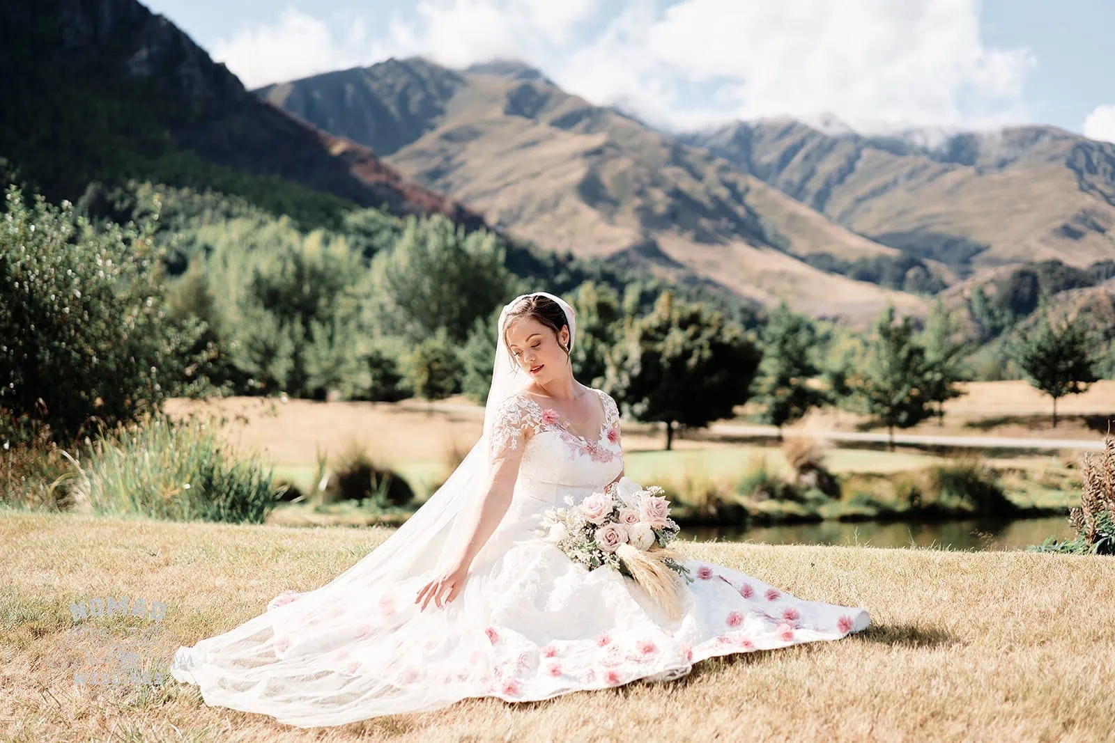Queenstown New Zealand Elopement Wedding Photographer - A bride sitting on the grass with mountains in the background at one of Queenstown's summer ground spots.