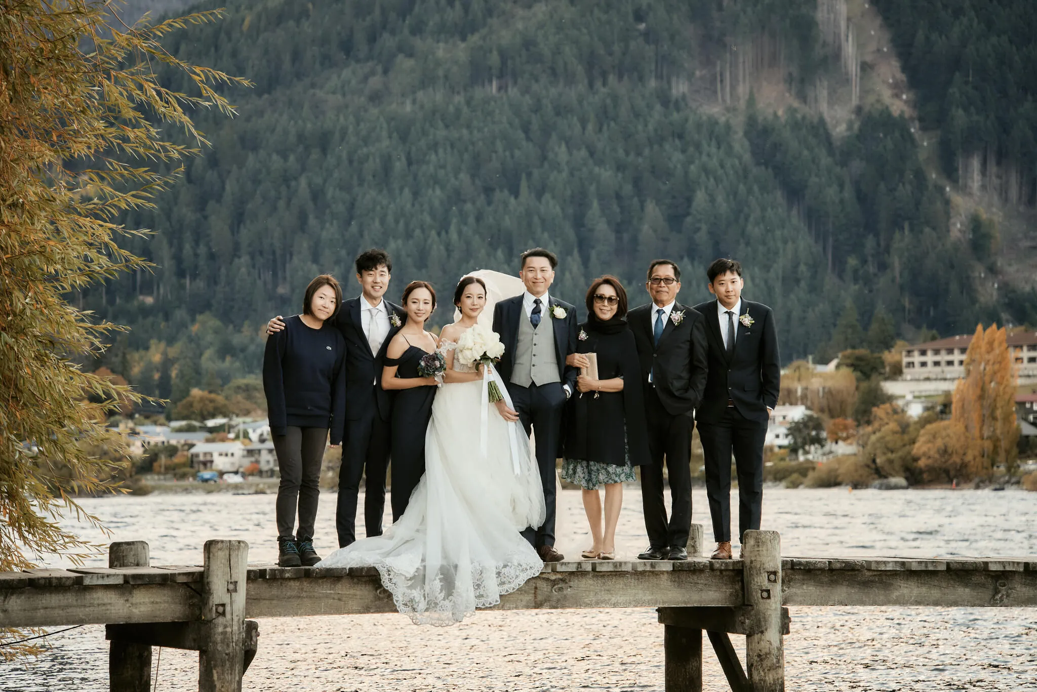 Queenstown New Zealand Elopement Wedding Photographer - Sarah and Tim's scenic Queenstown heli elopement wedding captured the couple and their wedding party posing on a dock with mountains in the background.