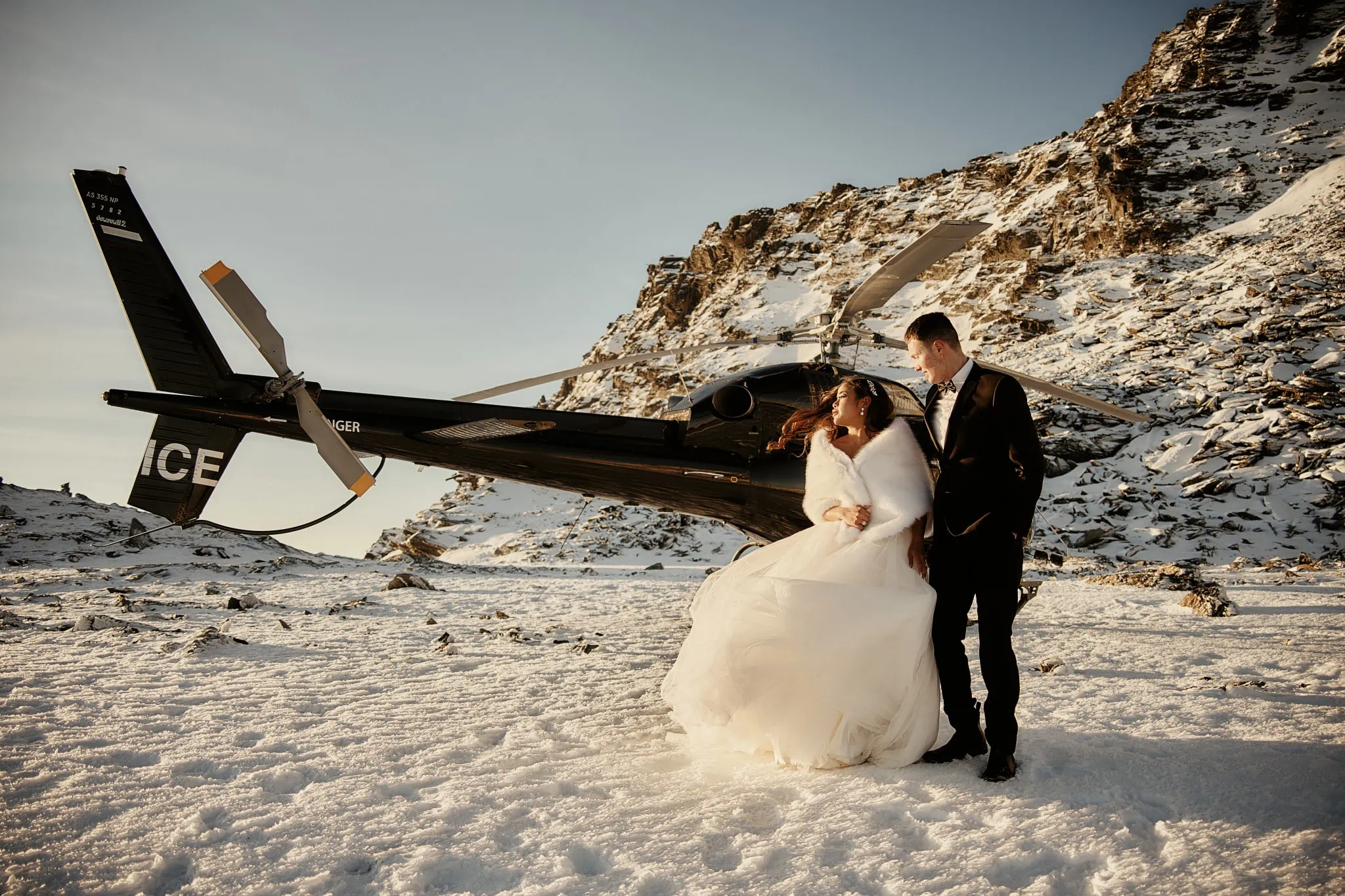 Queenstown New Zealand Elopement Wedding Photographer - Amy and Callum pose for a Queenstown Heli Pre Wedding Shoot, standing next to a helicopter in the beautiful snow.