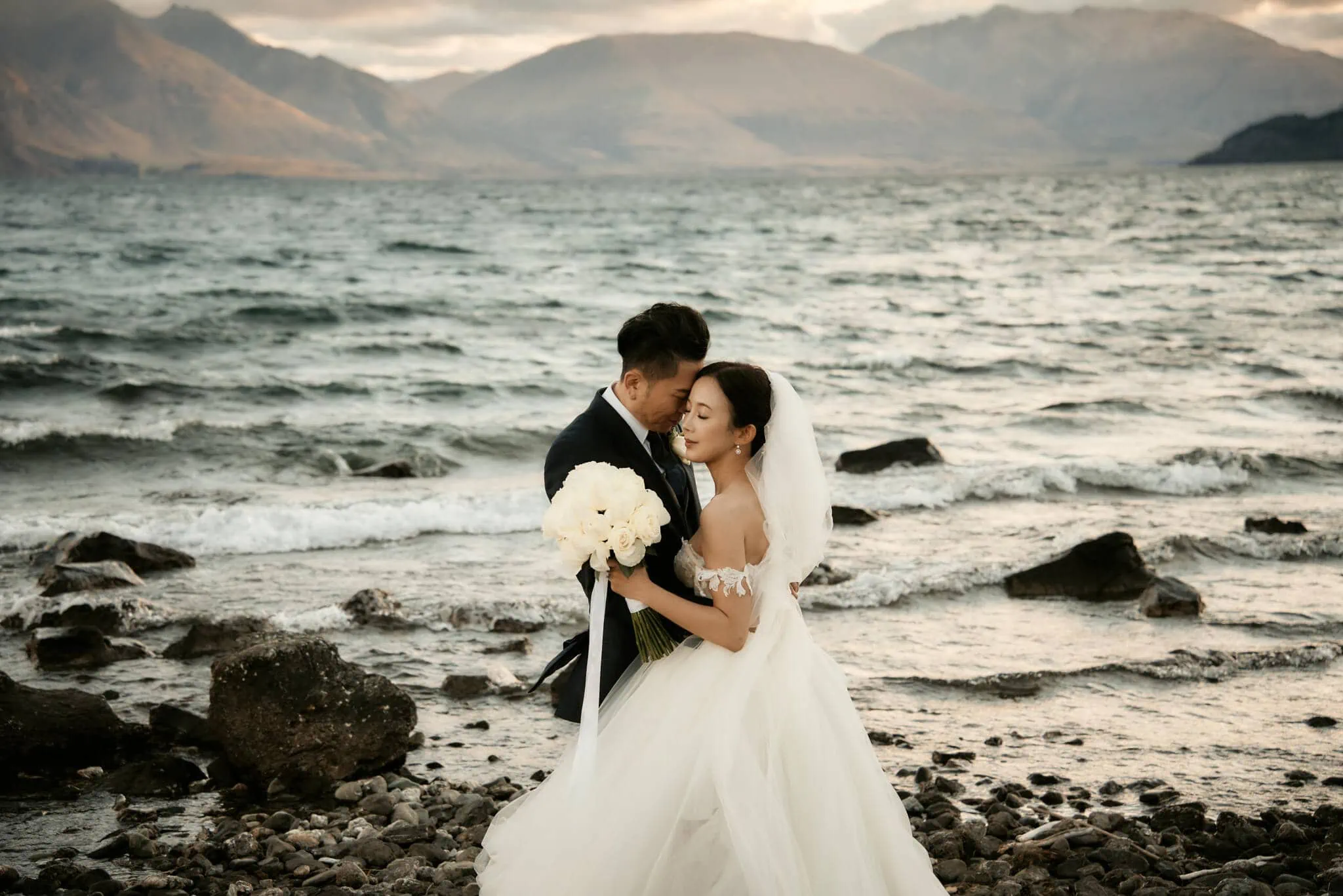 Queenstown New Zealand Elopement Wedding Photographer - A breathtaking elopement wedding featuring Sarah and Tim embracing on the shores of Lake Wanaka.