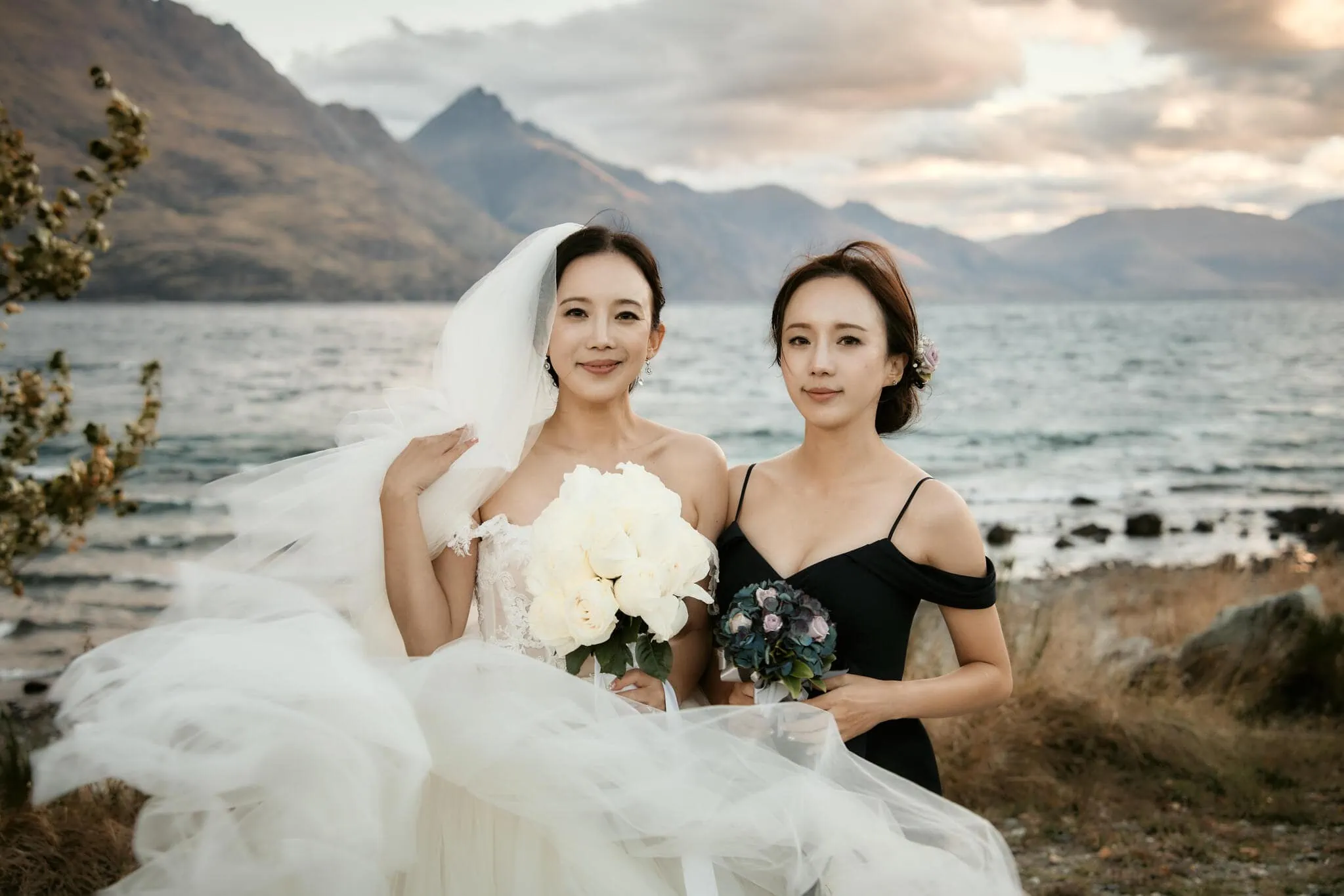 Queenstown New Zealand Elopement Wedding Photographer - Two brides posing in front of a scenic lake during their Queenstown heli elopement wedding in New Zealand.