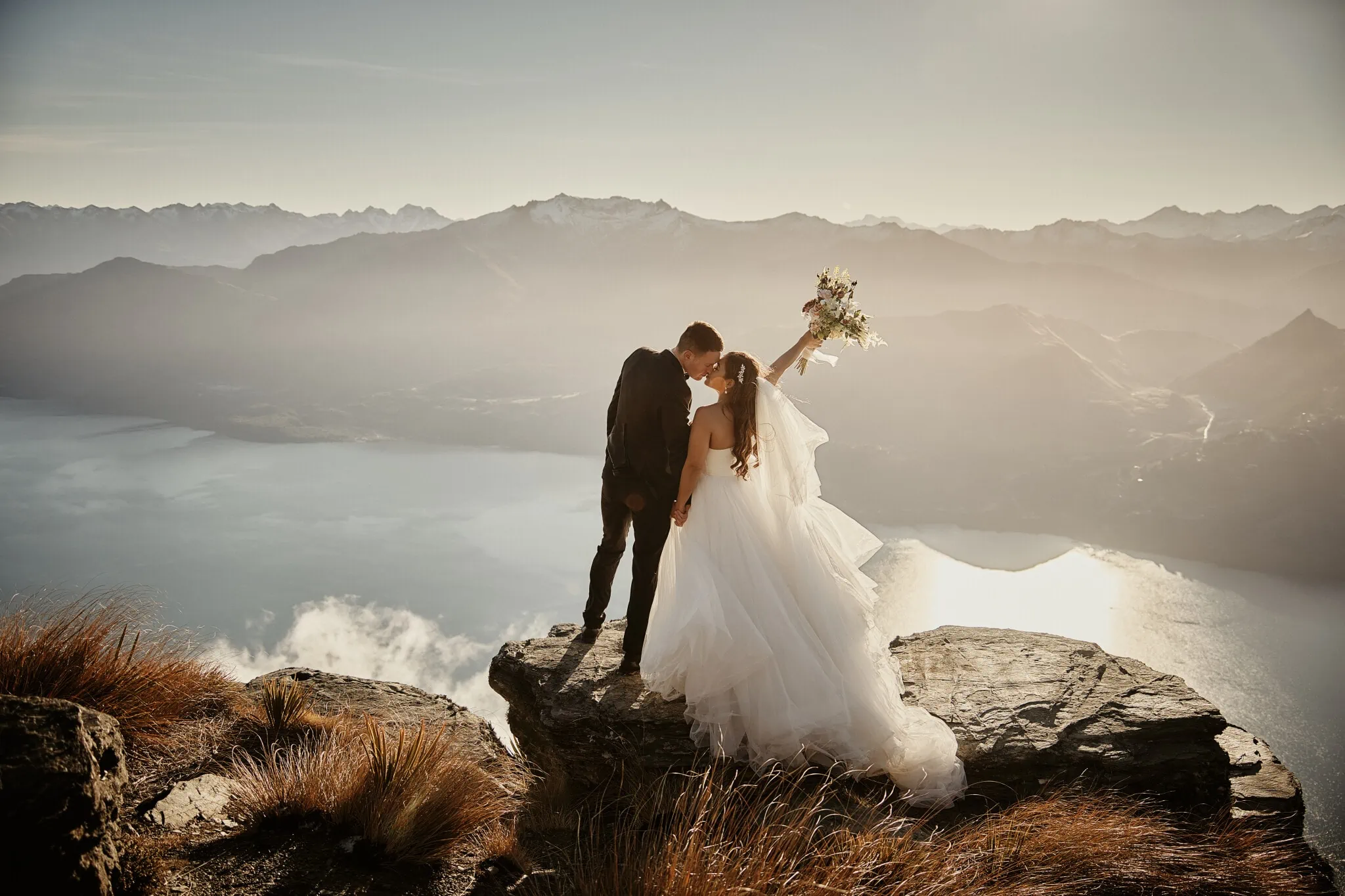 Queenstown New Zealand Elopement Wedding Photographer - Amy and Callum, a bride and groom, having a Queenstown Heli Pre Wedding Shoot on top of a cliff overlooking lake Wanaka.