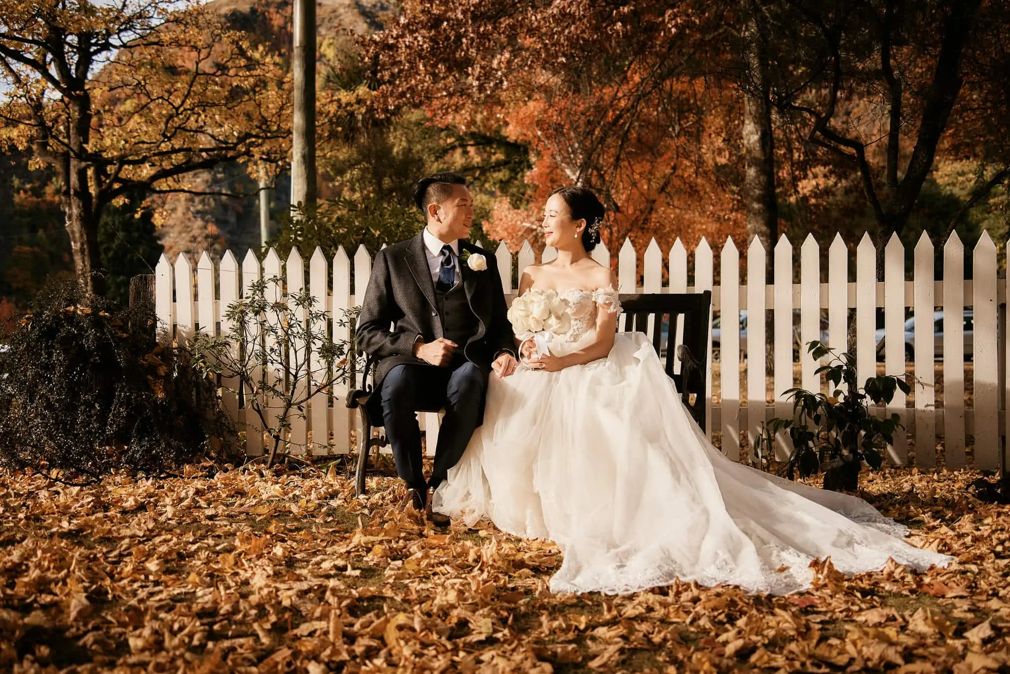 Queenstown New Zealand Elopement Wedding Photographer - Sarah and Tim's scenic Queenstown heli elopement wedding captured them sitting on a bench in autumn leaves.