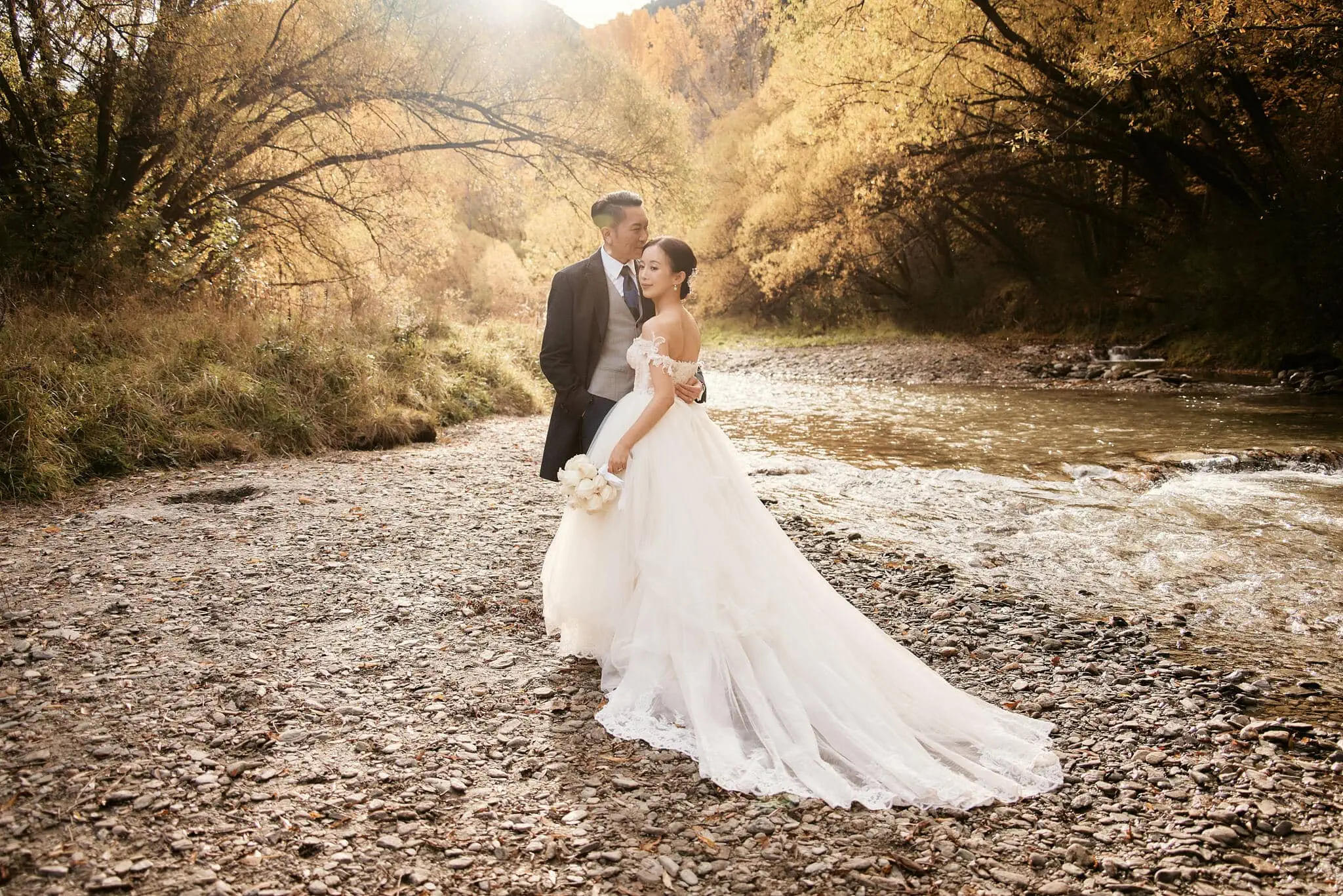 Queenstown New Zealand Elopement Wedding Photographer - Sarah and Tim, a bride and groom, standing next to a river in autumn during their Scenic Queenstown Heli Elopement Wedding.