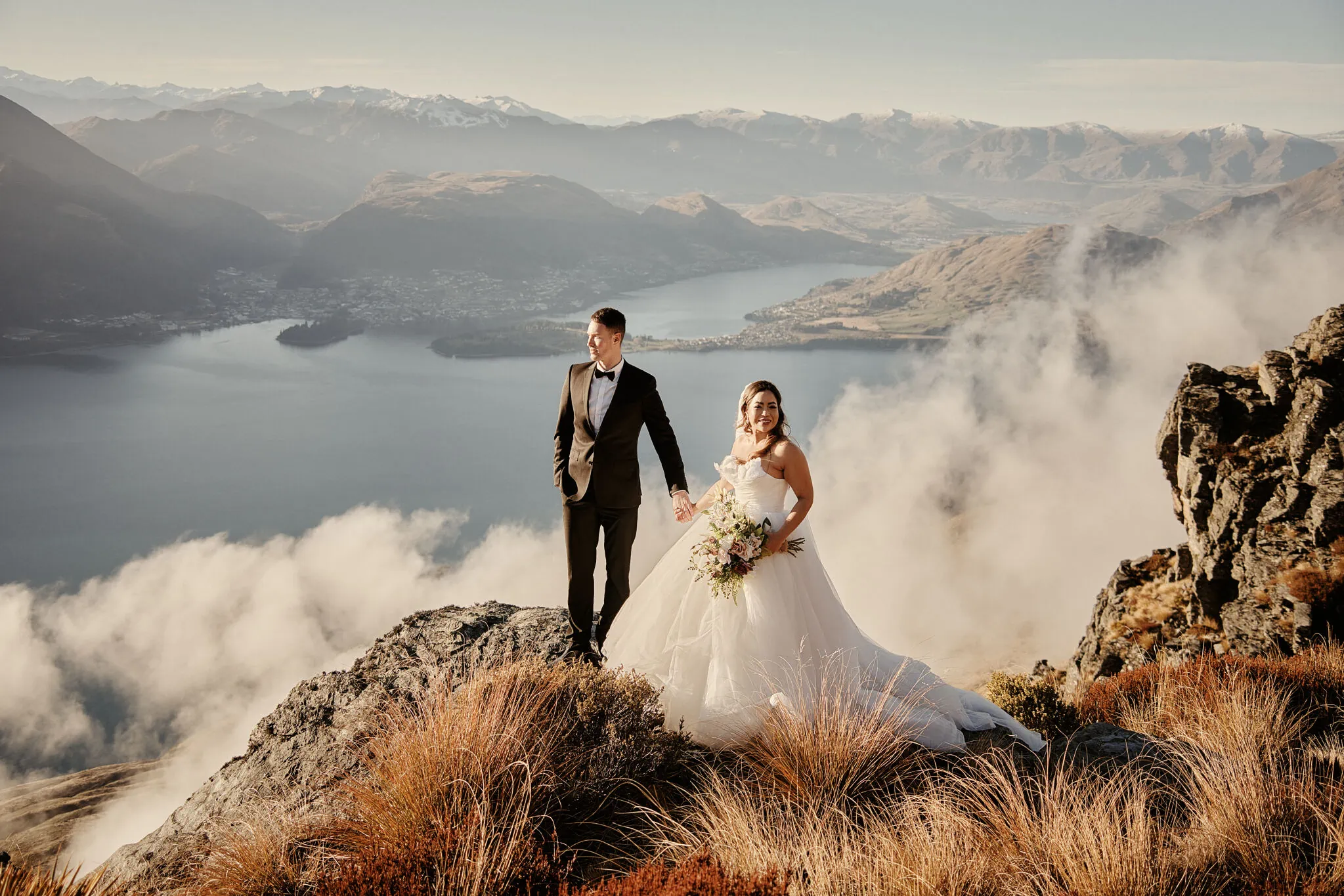 Queenstown New Zealand Elopement Wedding Photographer - Amy and Callum's Queenstown Heli Pre Wedding Shoot captures the couple standing on top of a mountain overlooking Lake Wanaka.