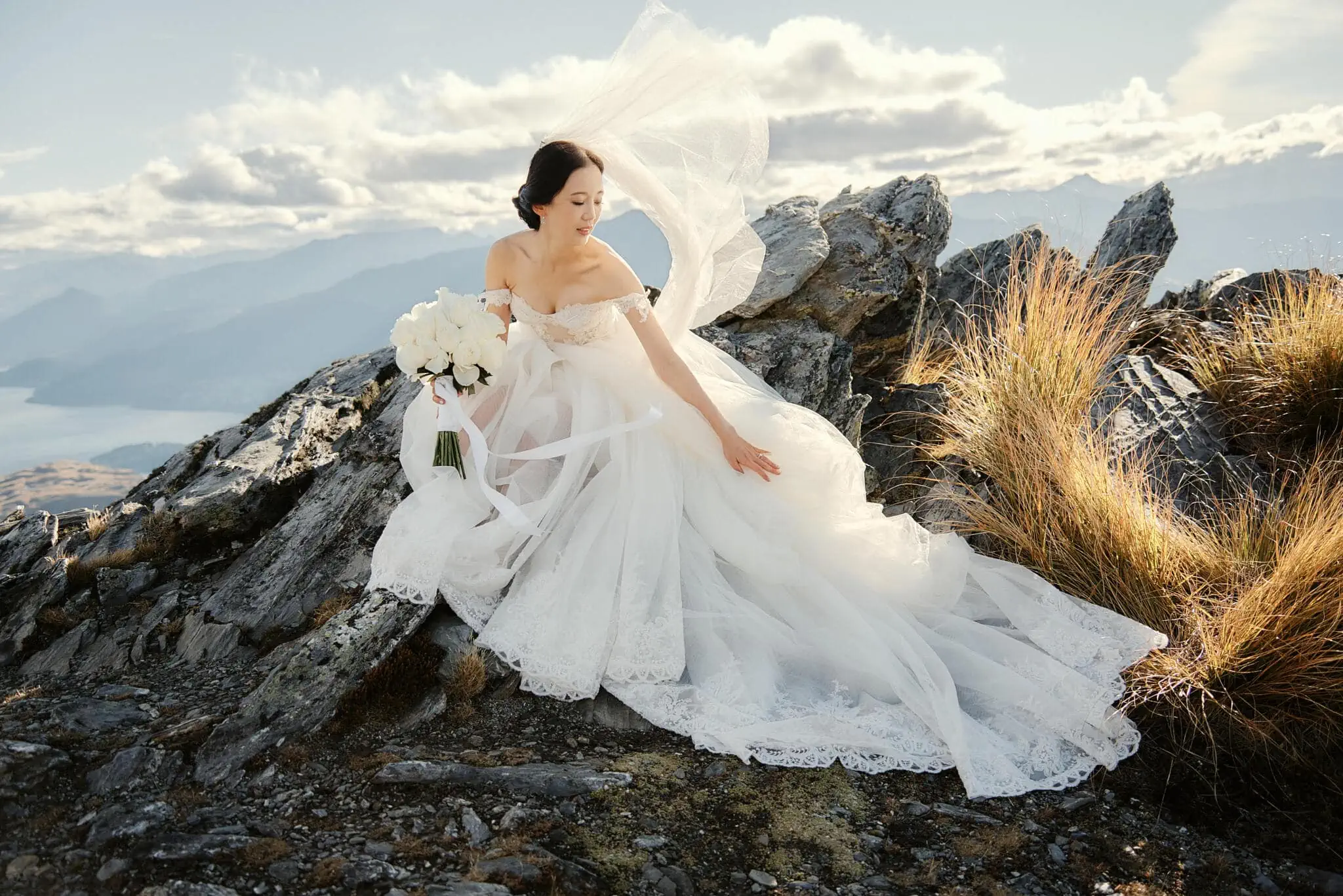 Queenstown New Zealand Elopement Wedding Photographer - Sarah and Tim's scenic Queenstown heli elopement wedding captures a breathtaking moment as the bride sits atop a mountain surrounded by majestic peaks.