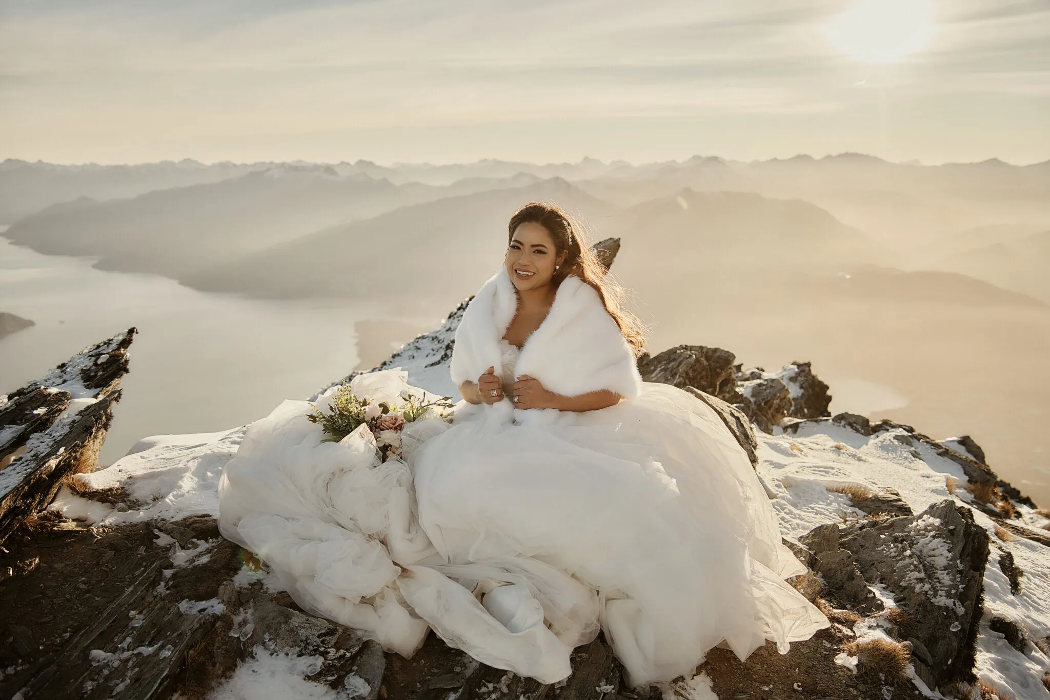 Queenstown New Zealand Elopement Wedding Photographer - Amy and Callum capture stunning pre-wedding moments as they sit atop a picturesque mountain in Queenstown, adorned in a white dress.