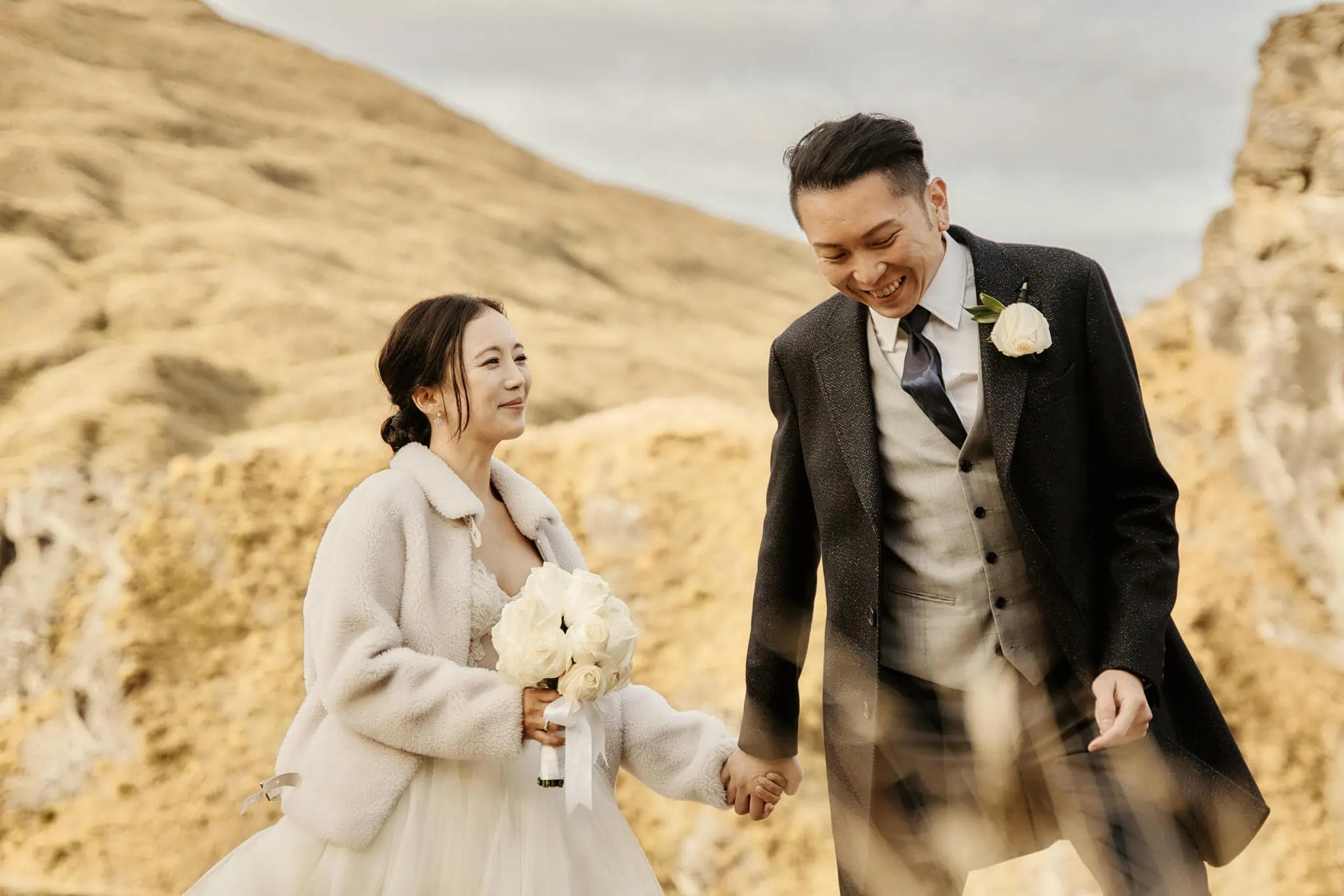 Queenstown New Zealand Elopement Wedding Photographer - Sarah and Tim's scenic Queenstown heli elopement wedding: A couple holding hands in a grassy field.