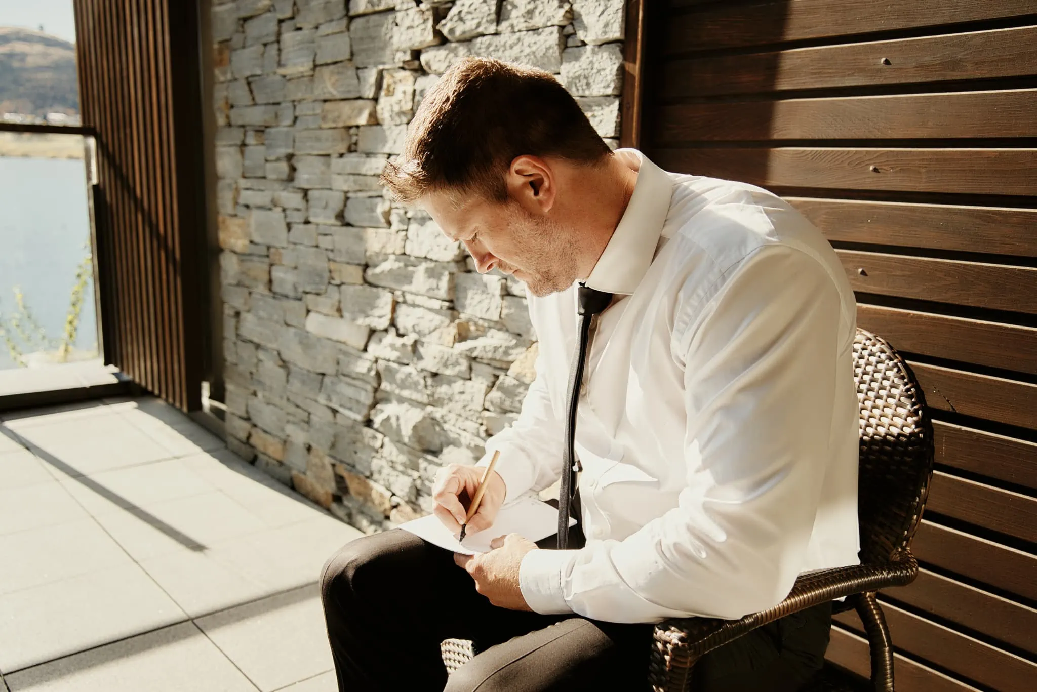 Queenstown New Zealand Elopement Wedding Photographer - A man sitting in a chair writing a note during Ashleigh and Anthony's Roy's Peak Heli Elopement Wedding.