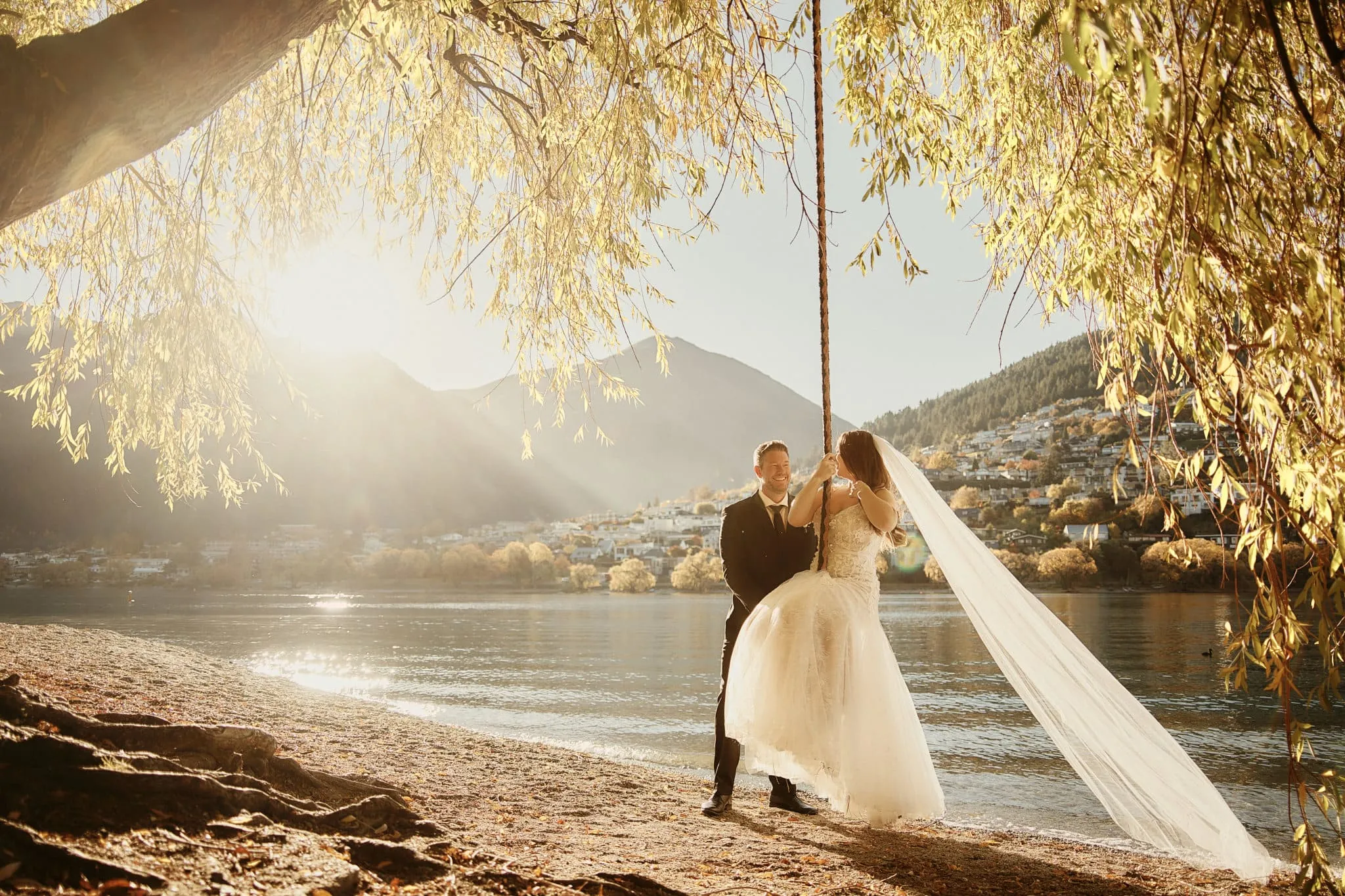Queenstown New Zealand Elopement Wedding Photographer - Ashleigh and Anthony's Roy's Peak Heli Elopement Wedding: A bride and groom standing under a willow tree on the shore of Lake Wanaka.